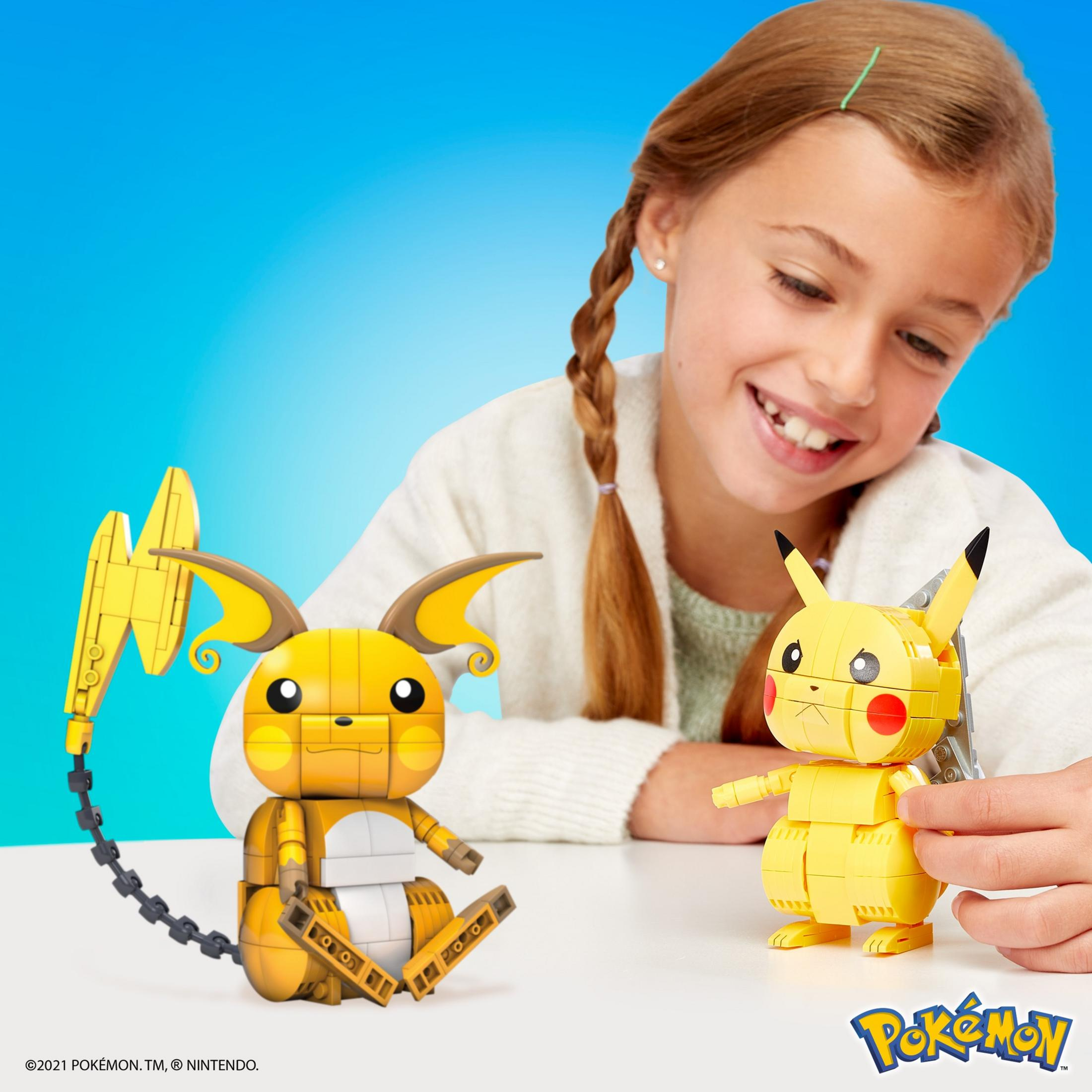 Uśmiechnięta dziewczyna z dwiema figurkami Lego Pokémon na białej powierzchni.