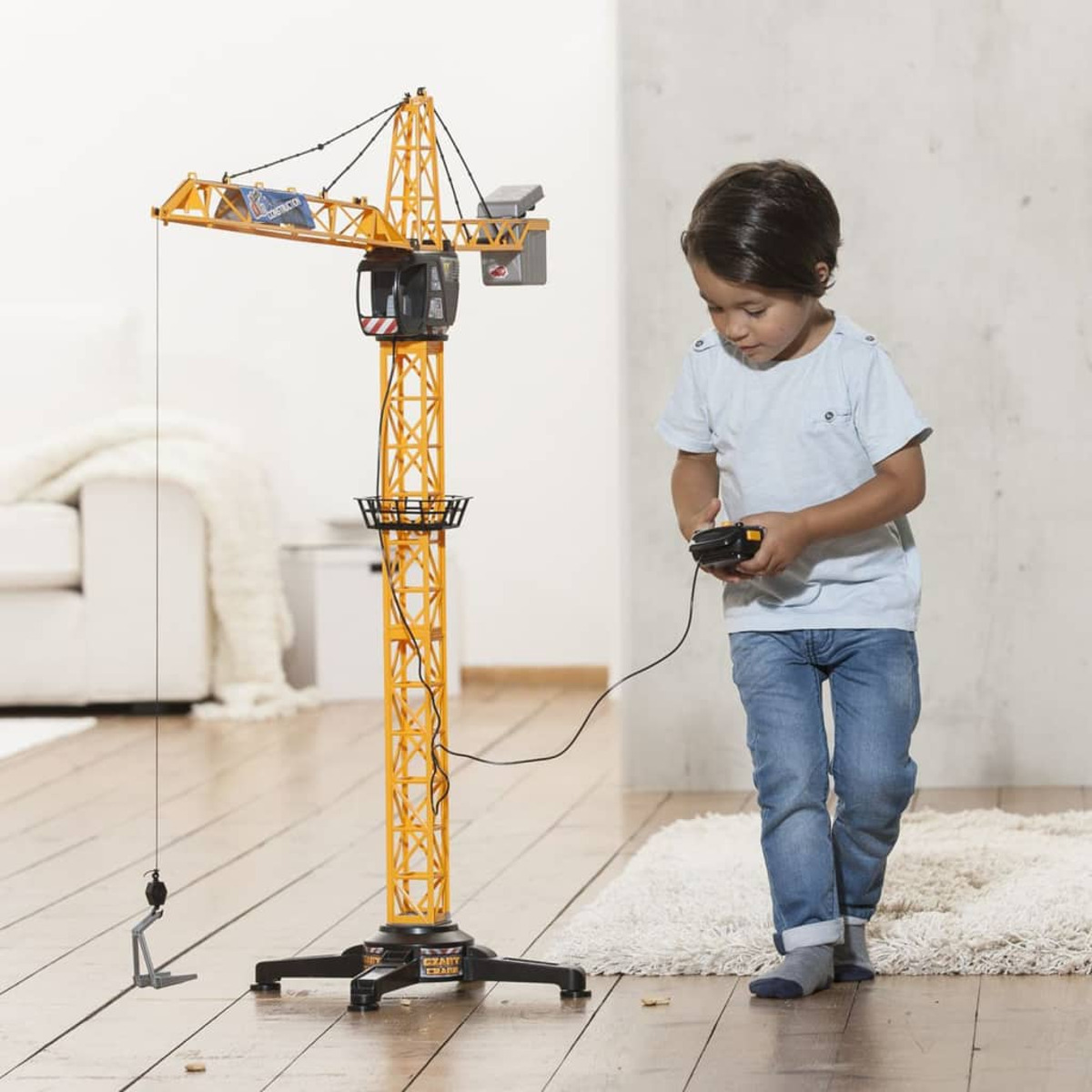 Ein Junge bedient einen großen gelben Spielzeugkran mit einer Fernbedienung.