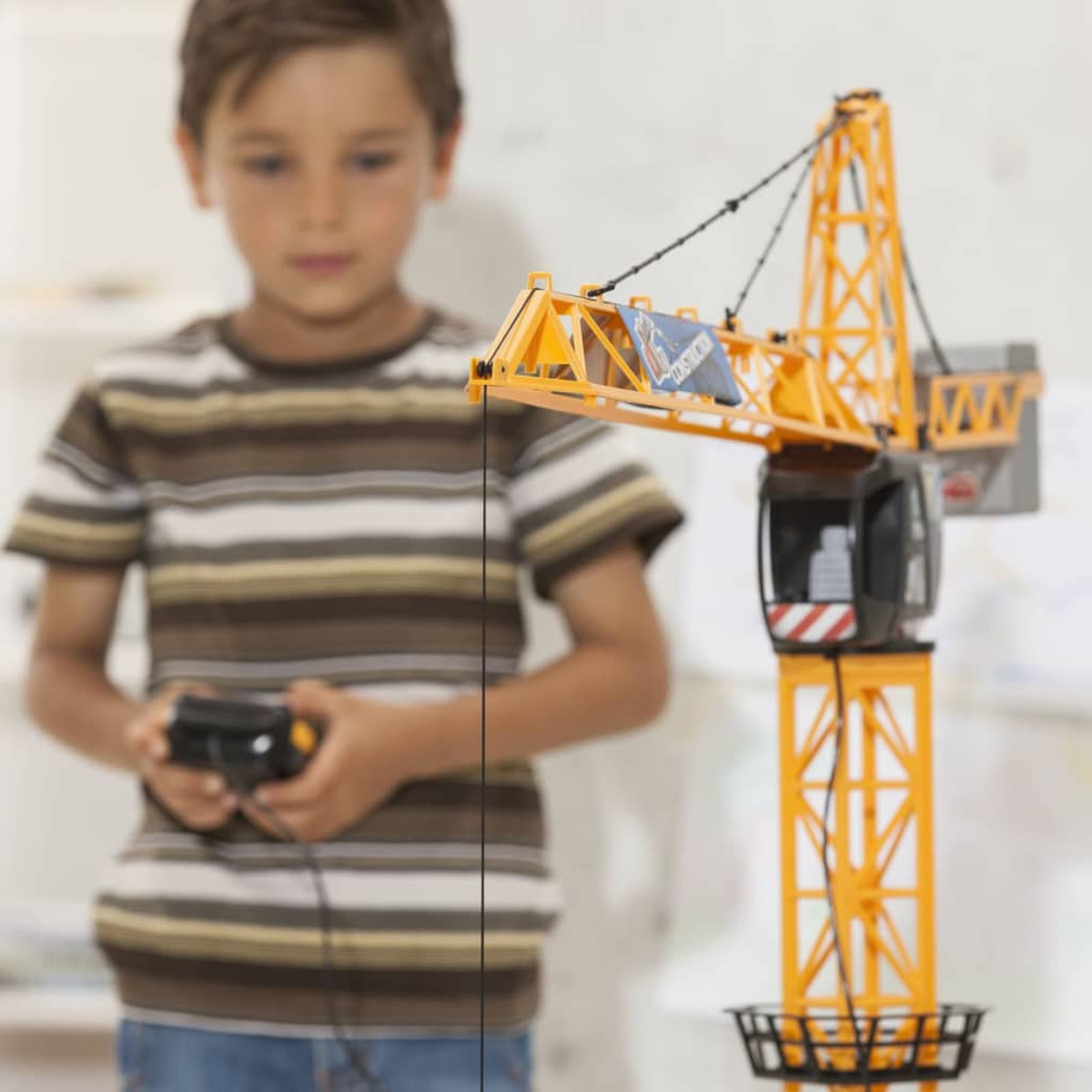 Ein Junge hält eine Fernbedienung und schaut auf einen gelb-orangen Spielzeugkran.