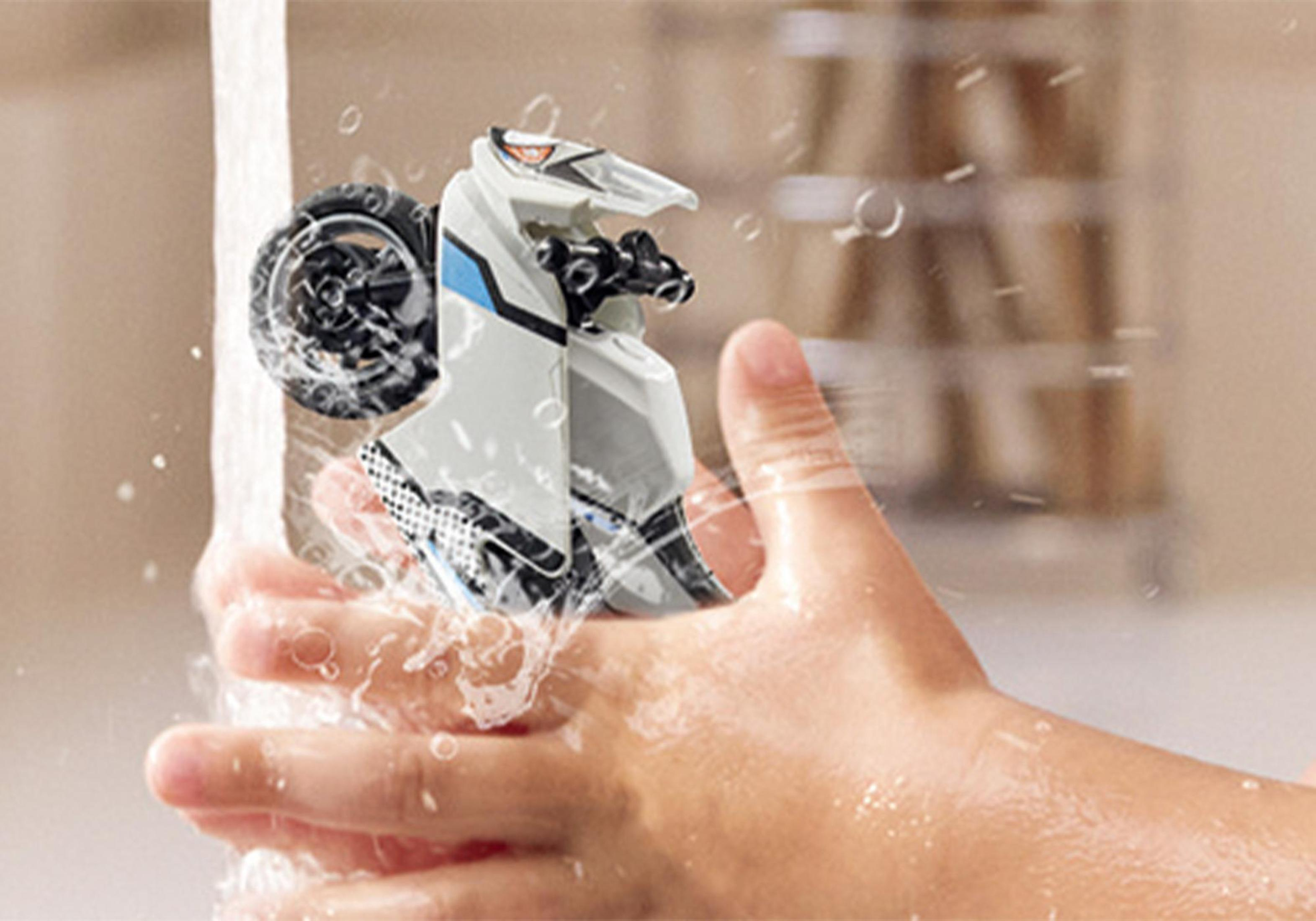 Ein Spielzeugmotorrad wird unter fließendem Wasser gereinigt. Das Motorrad ist weiß mit schwarzen und blauen Details.