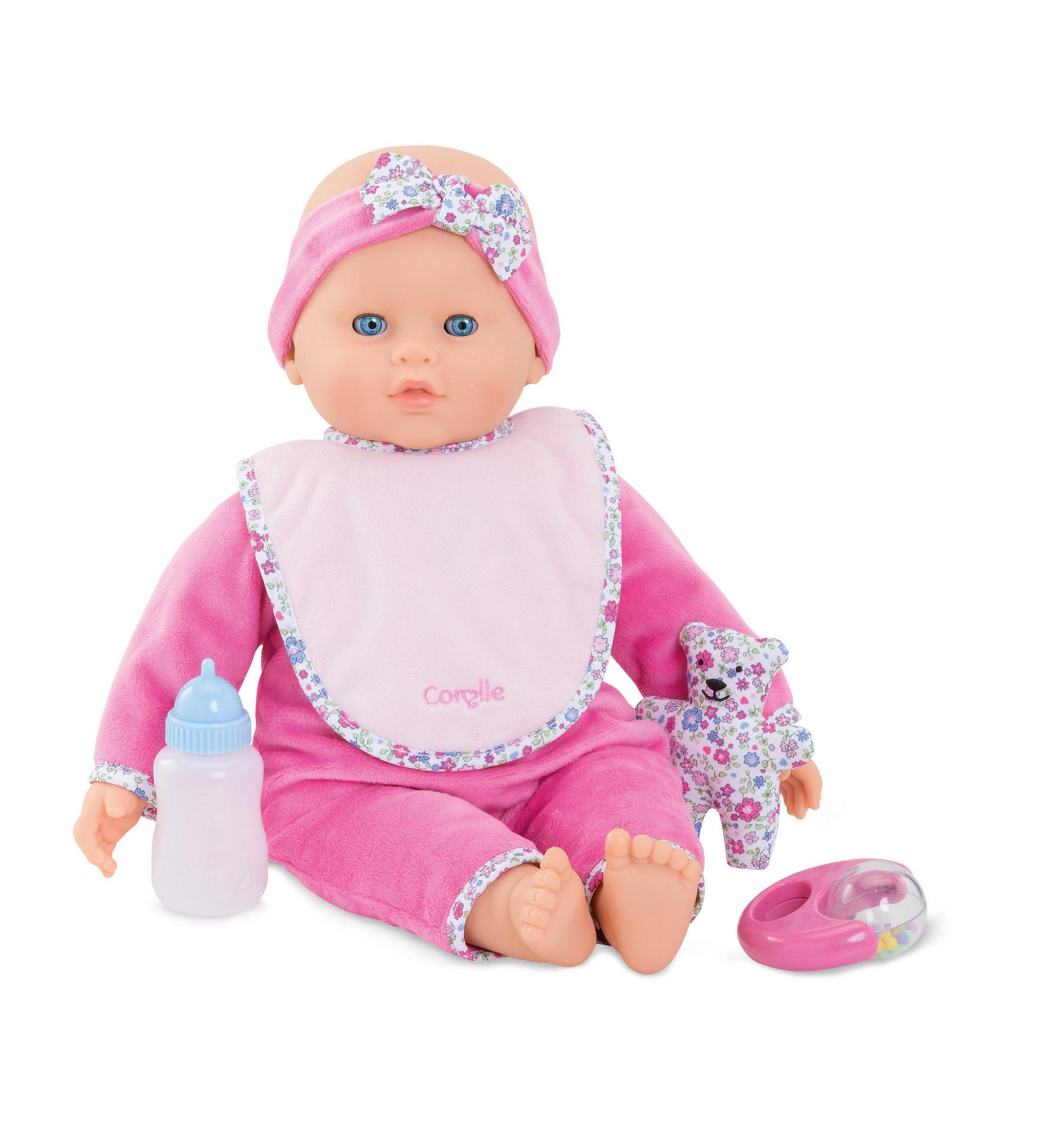 Eine Babypuppe mit rosa Kleidung, Flasche, Bär und Rassel. Weißer Hintergrund.