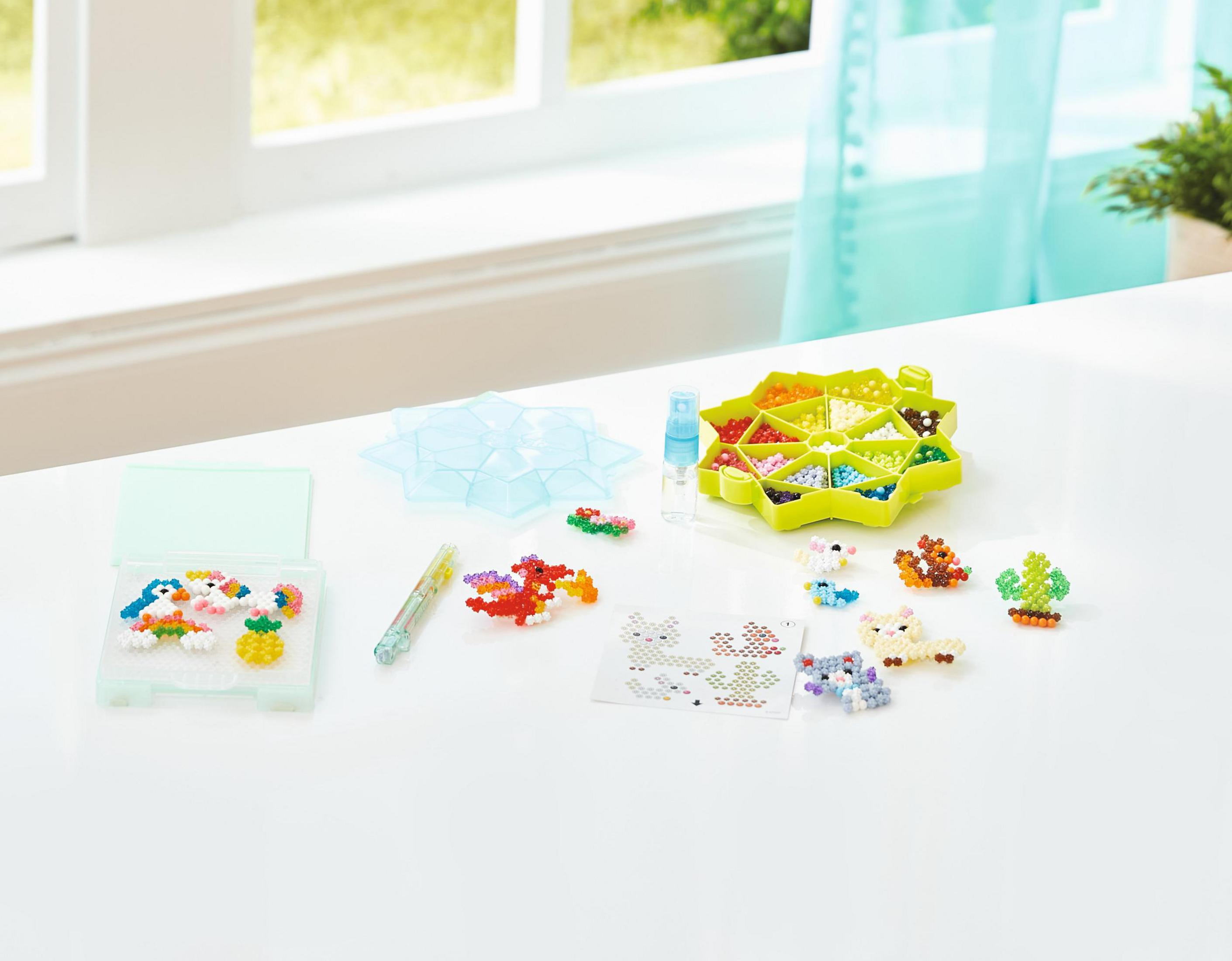 Set per l'artigianato con piccole figure e perline colorate, disposte su una superficie bianca.