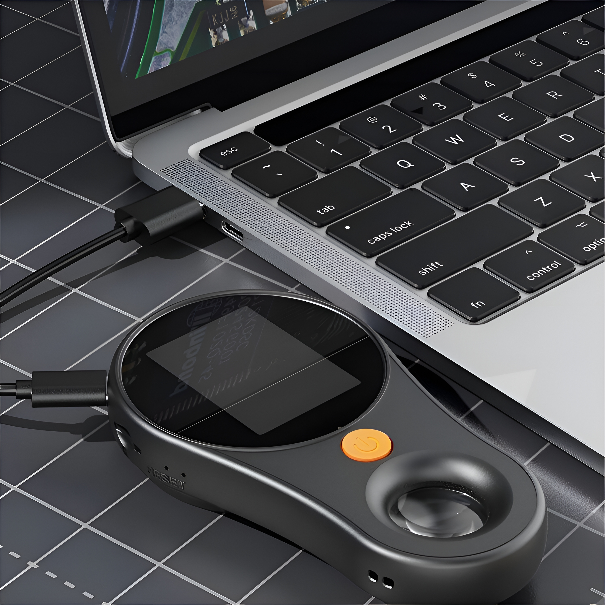 Ein Laptop, der mit einem Gerät mit Bildschirm und orangefarbenem Knopf verbunden ist. Schwarze Oberfläche.