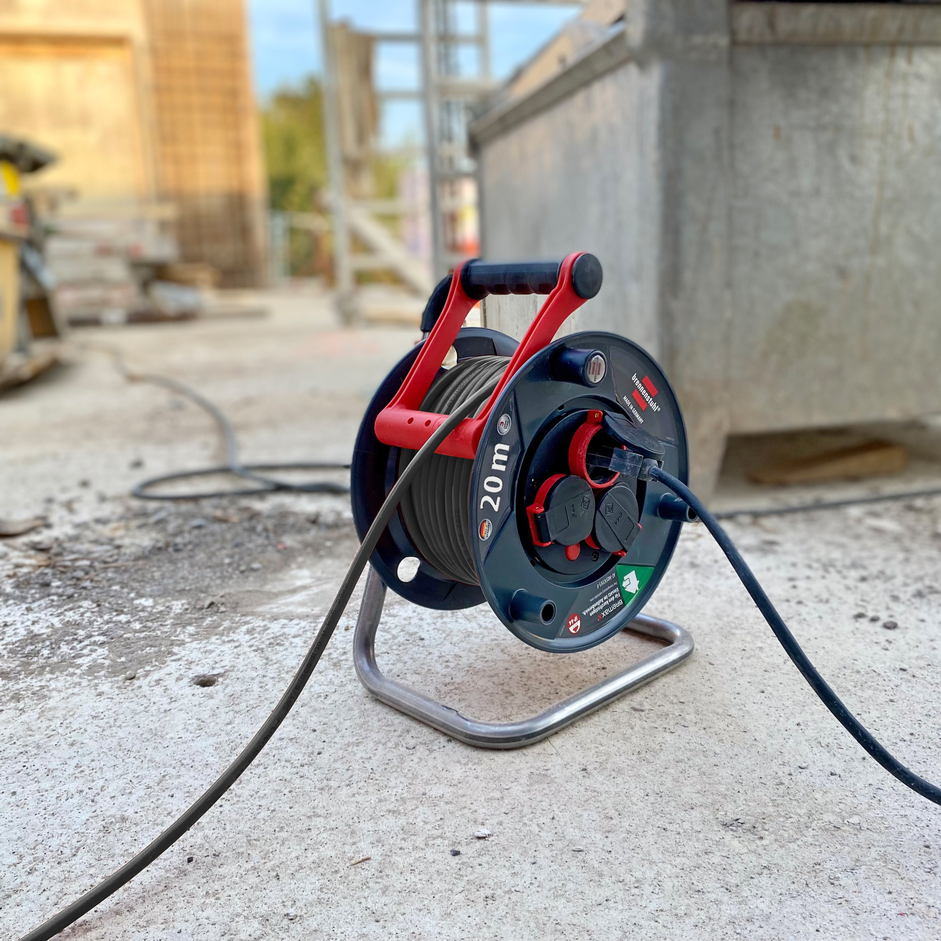 Eine schwarz-rote Kabeltrommel auf einer Baustelle. Der Hintergrund ist mit Baumaterialien verschwommen.