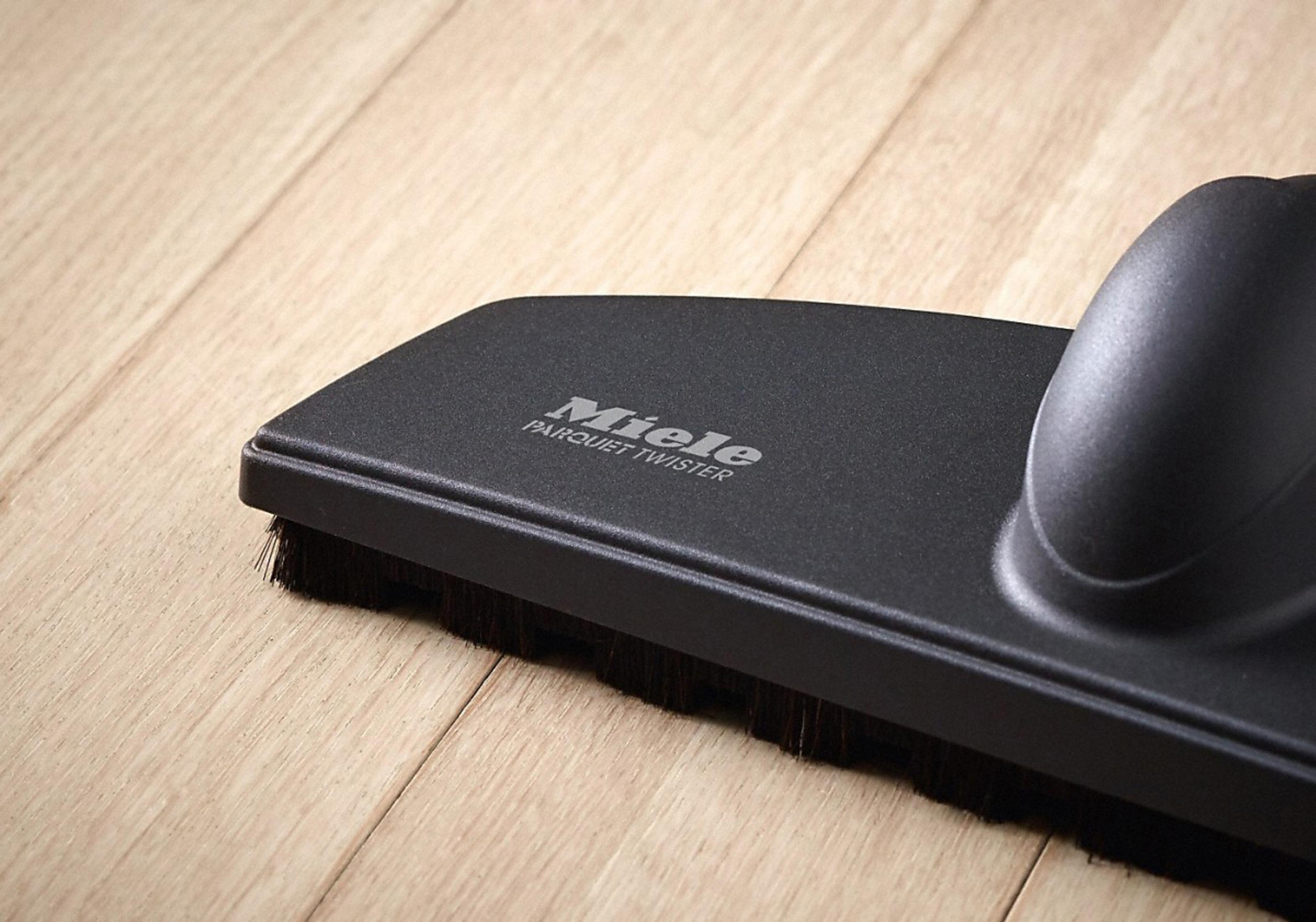 Czarna głowica odkurzacza na jasnej drewnianej podłodze.