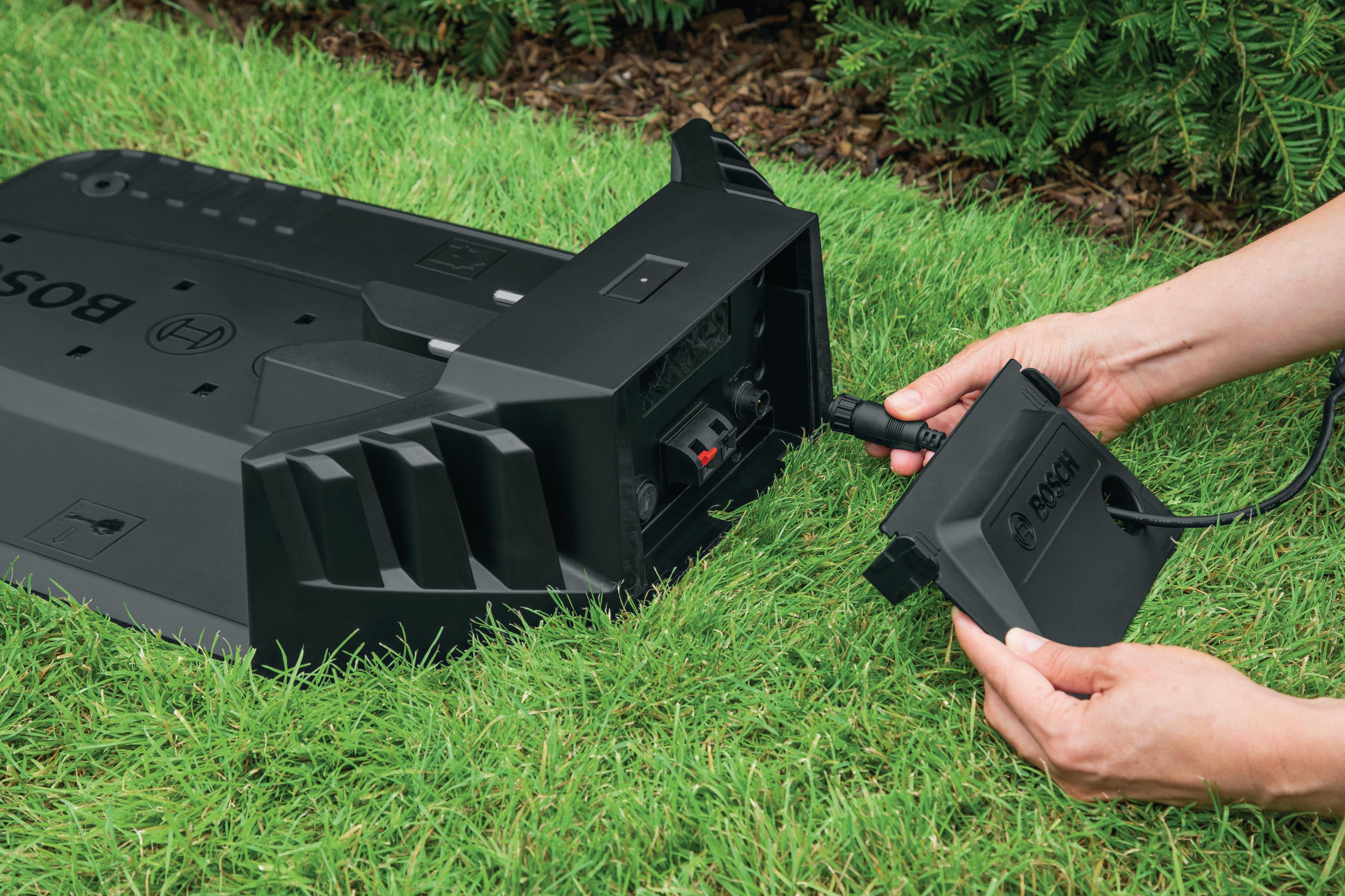 Ręce podłączające kabel ładujący do czarnej kosiarki robotycznej.