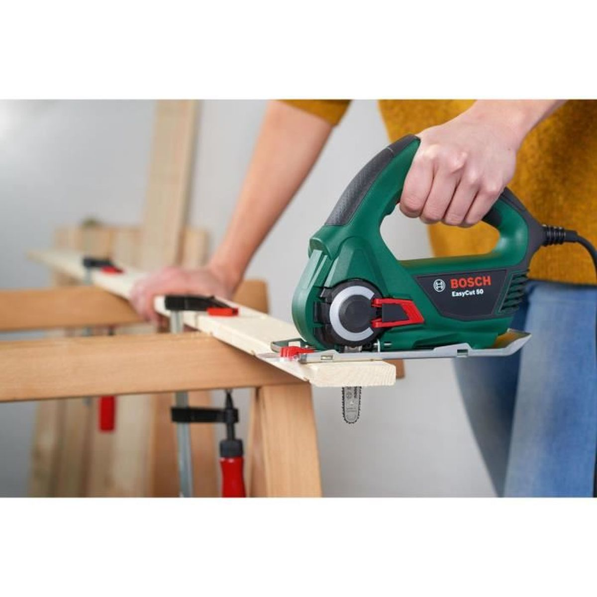 Persona che usa una sega verde e nera per tagliare un'asse di legno.