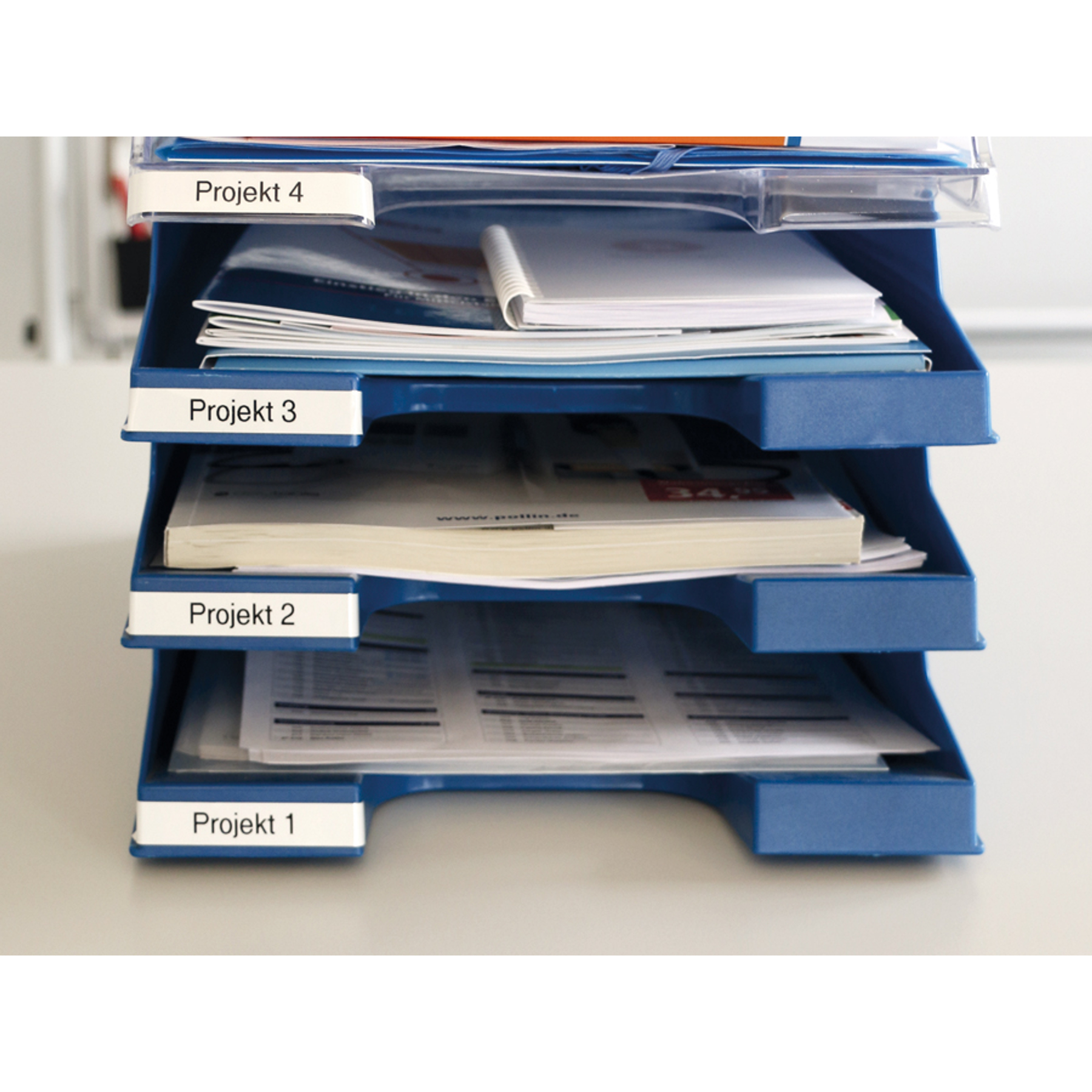 Gestapelte blaue Ablagen mit beschrifteten Dokumenten; beschriftet mit 'Projekt 1-4'.
