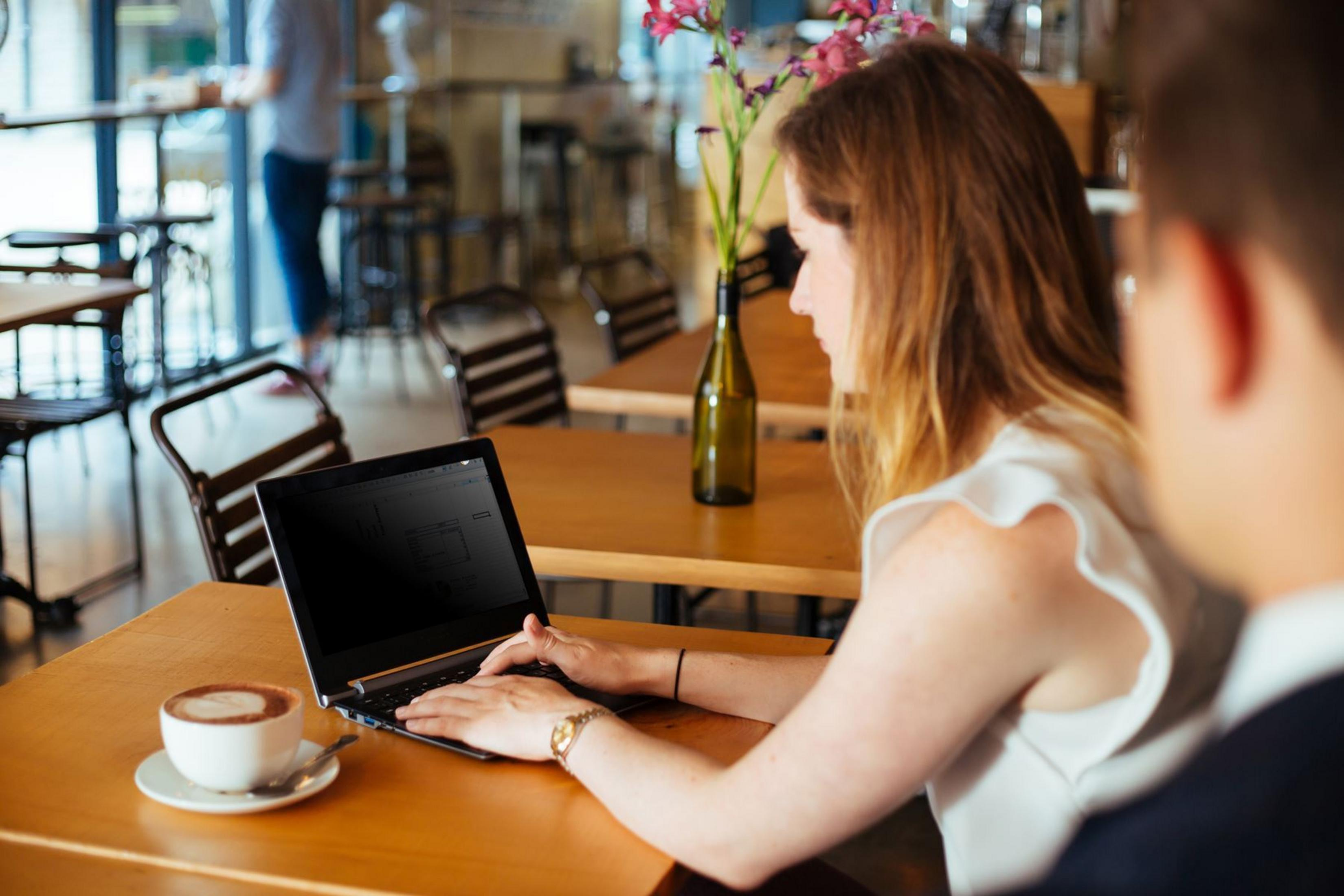 Frau benutzt Laptop in einem Café, mit Kaffee und Blumen.