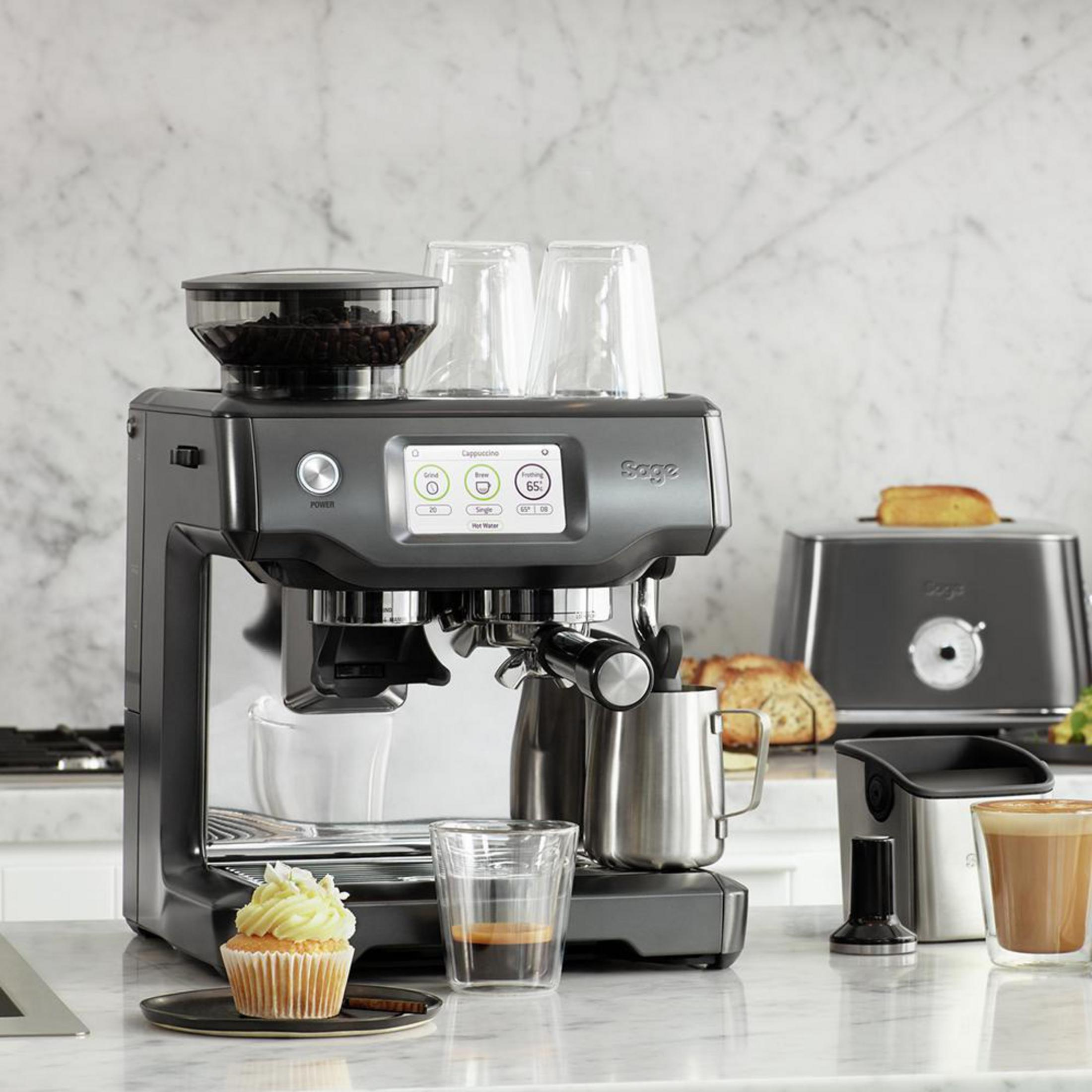 Ekspres do kawy z akcesoriami na marmurowym blacie. Zawiera babeczkę i szklanki.