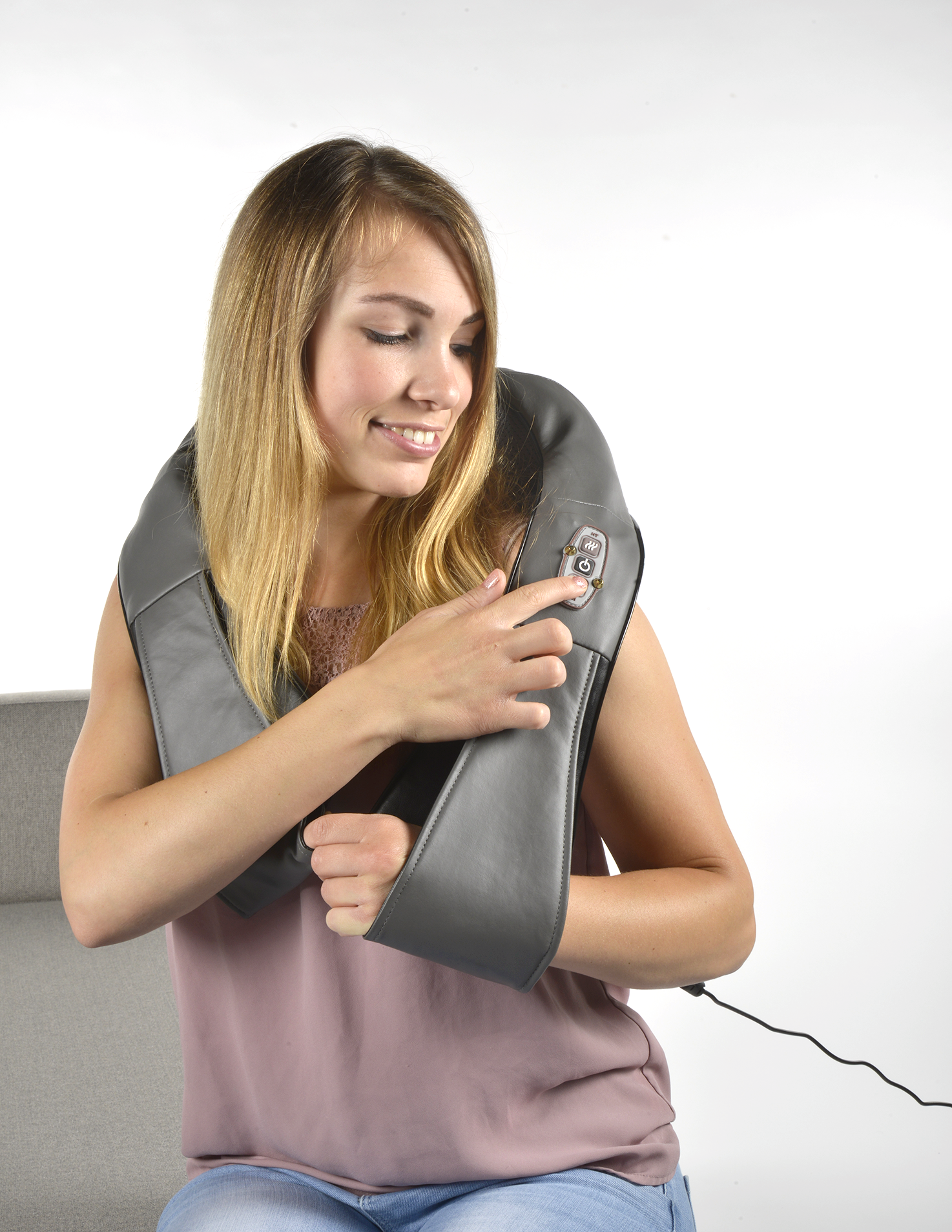 A woman uses a neck massager, smiling, white background.