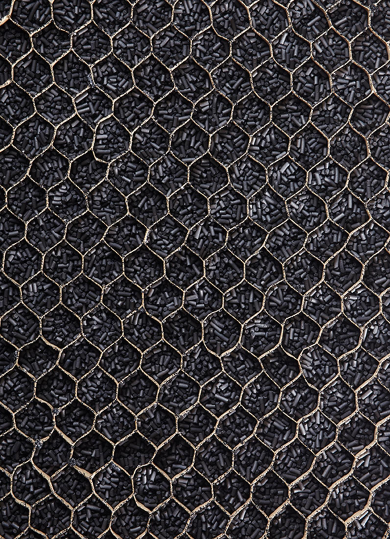 Nahaufnahme eines schwarzen Luftfilters mit goldenem Metallgitter, gefüllt mit schwarzen Granulaten.