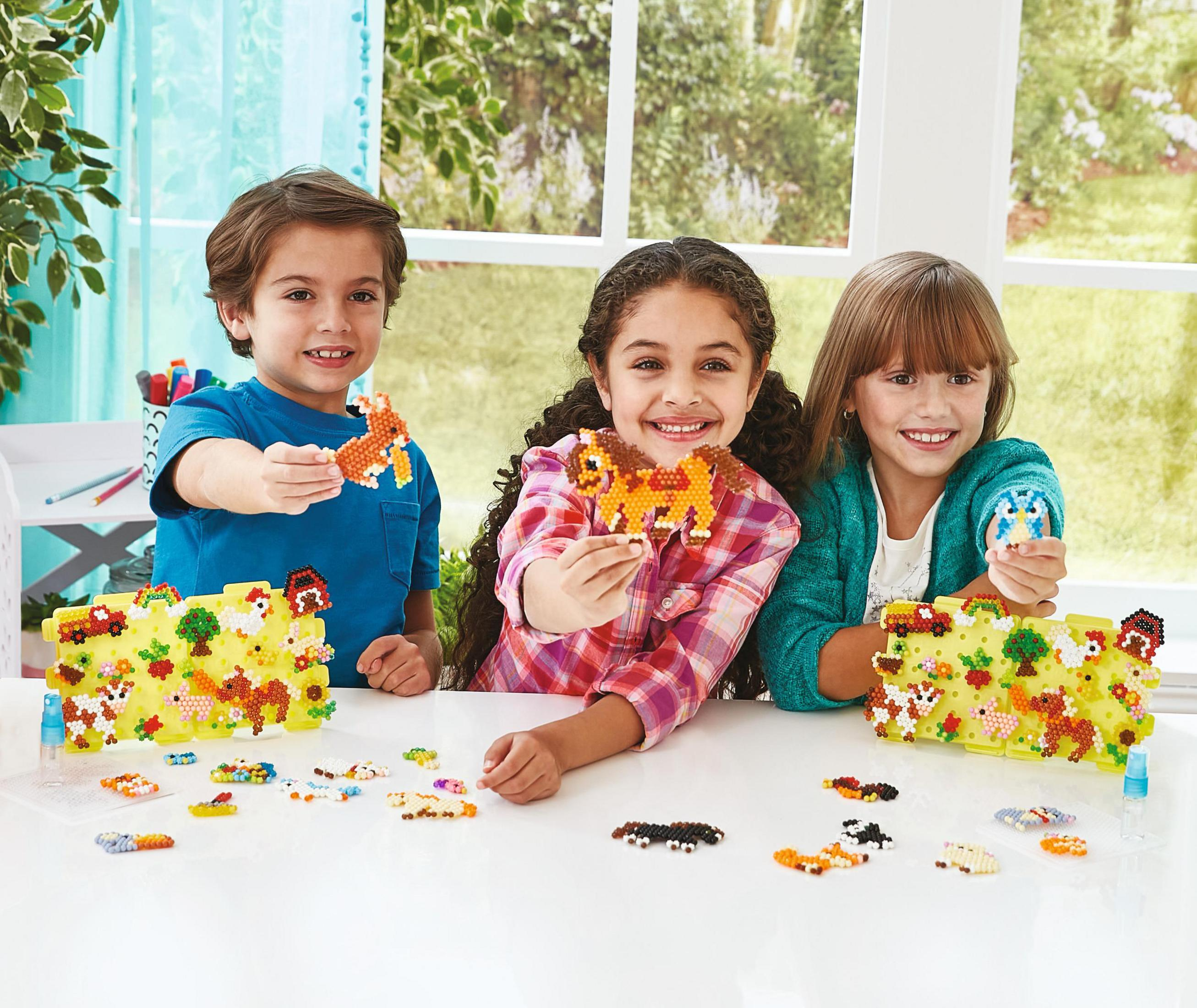Tres niños sonriendo, sosteniendo arte de cuentas, sentados en una mesa.