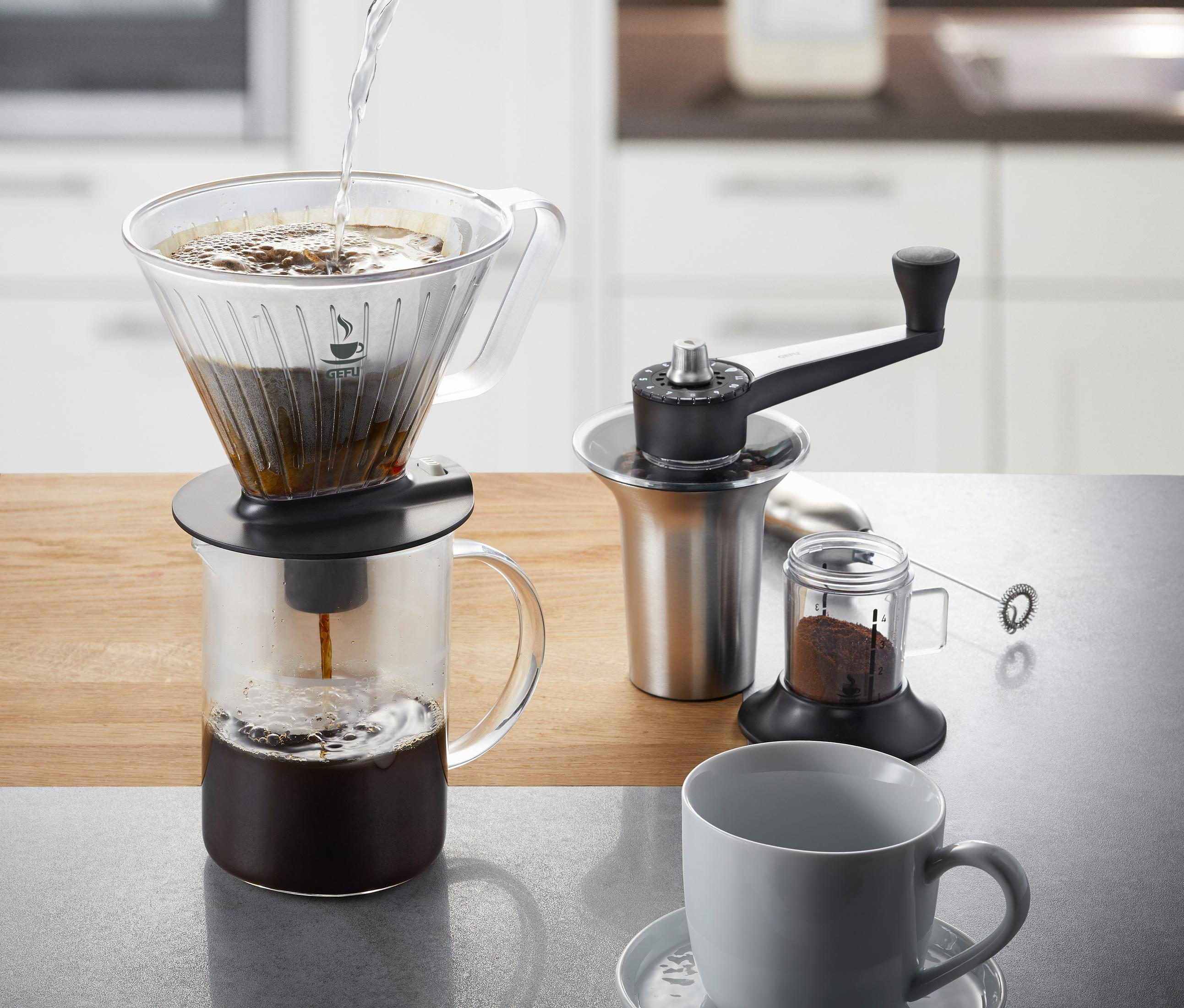 Kaffeezubereitung. Glas-Dripper, Mühle und Tasse. Wasser gießen. Weiße Arbeitsplatte.