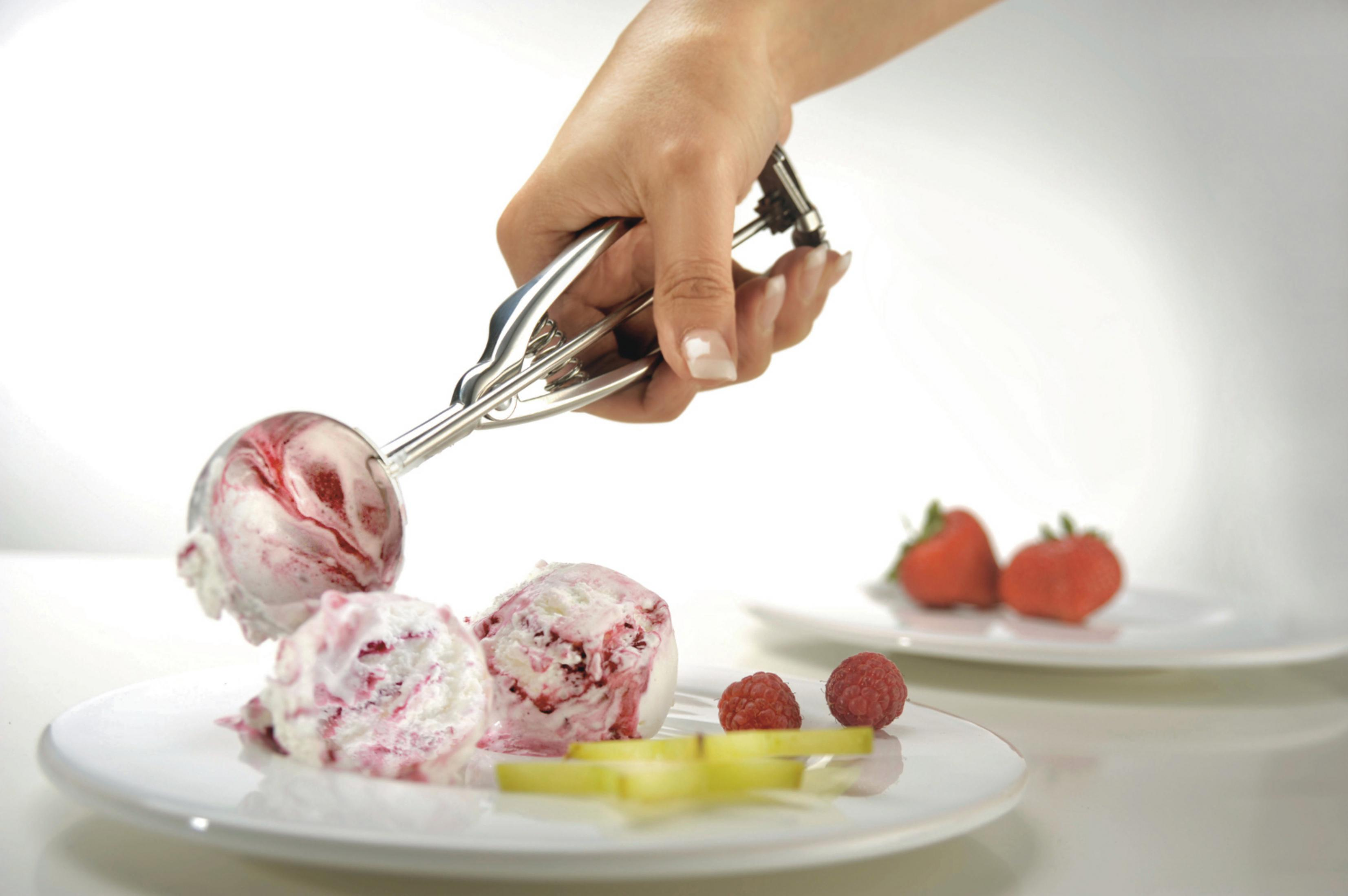 Eine Hand schöpft Eiscreme auf einen Teller mit Beeren und Obst.