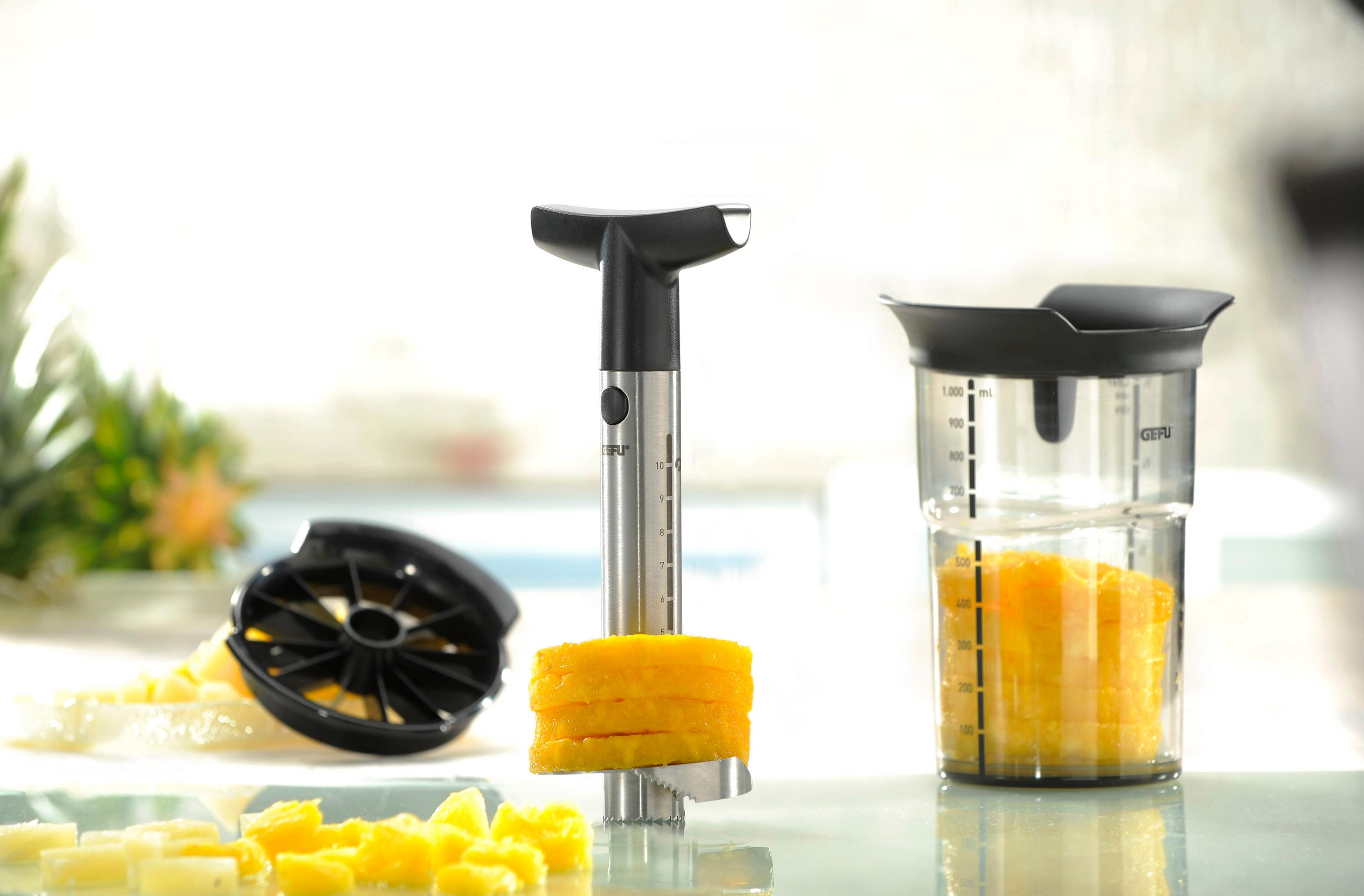 Ein GEFU Ananasschneider mit geschnittener Ananas und einem Messbecher mit Ananassaft. Es ist auf weißem Untergrund.