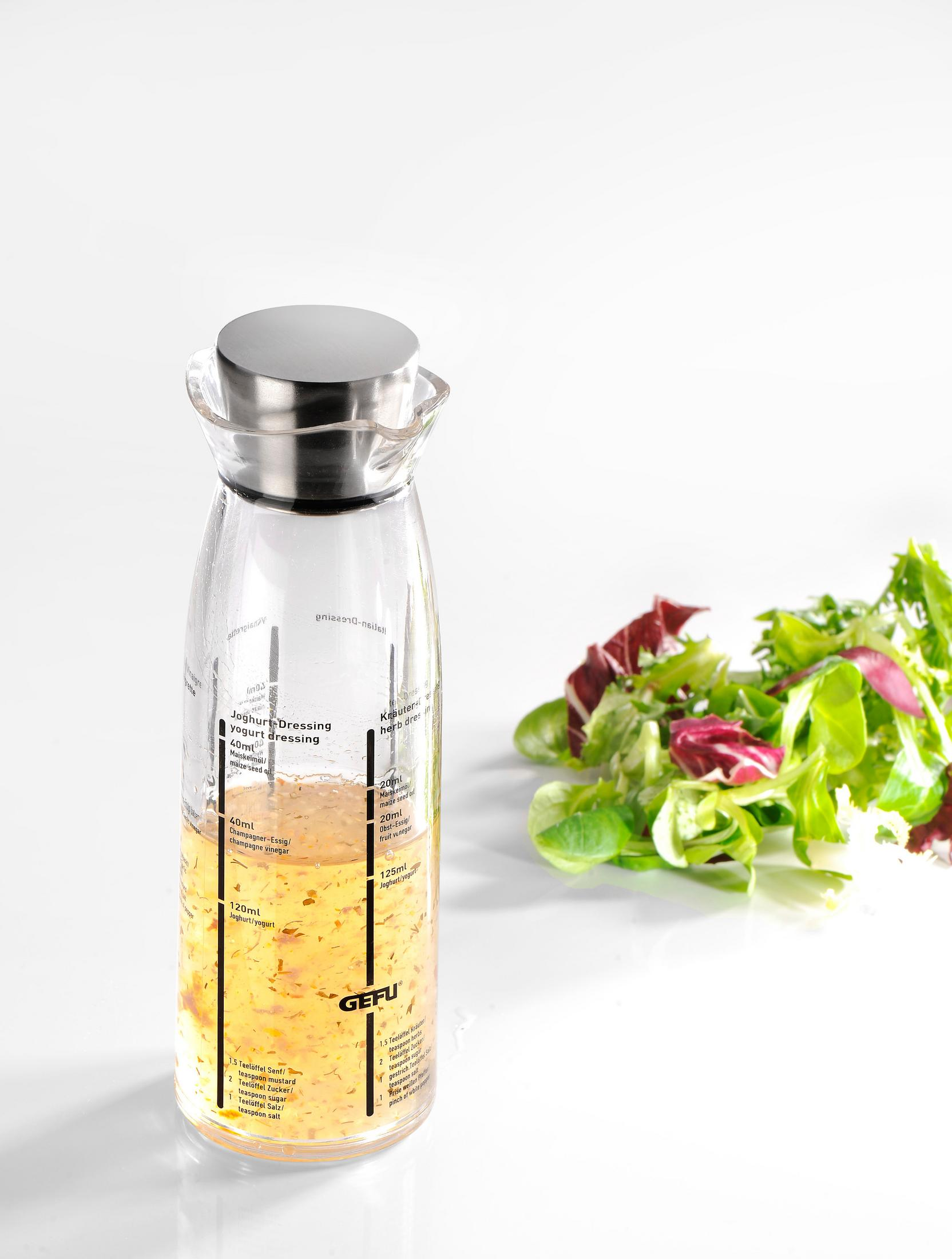 Eine Glas-Salatdressing-Flasche mit Skala und Salat daneben.