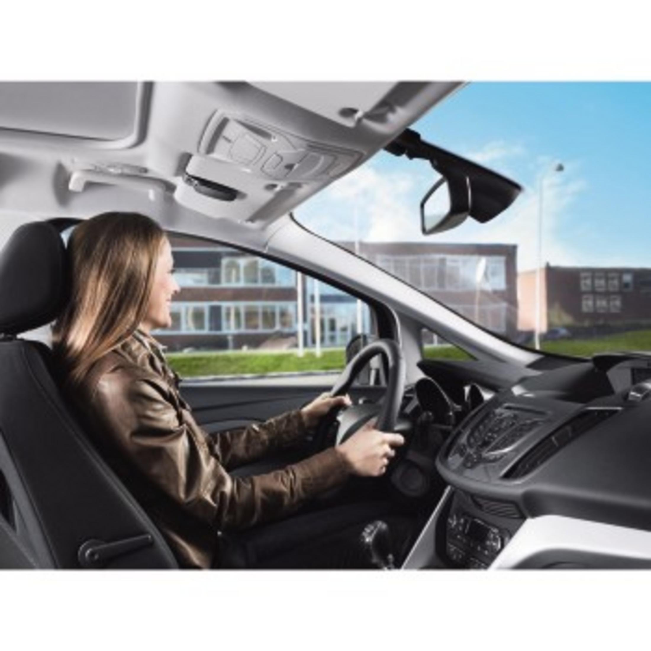 Eine Frau fährt Auto, blickt nach rechts, mit blauem Himmel im Hintergrund. Im Inneren des Autos.