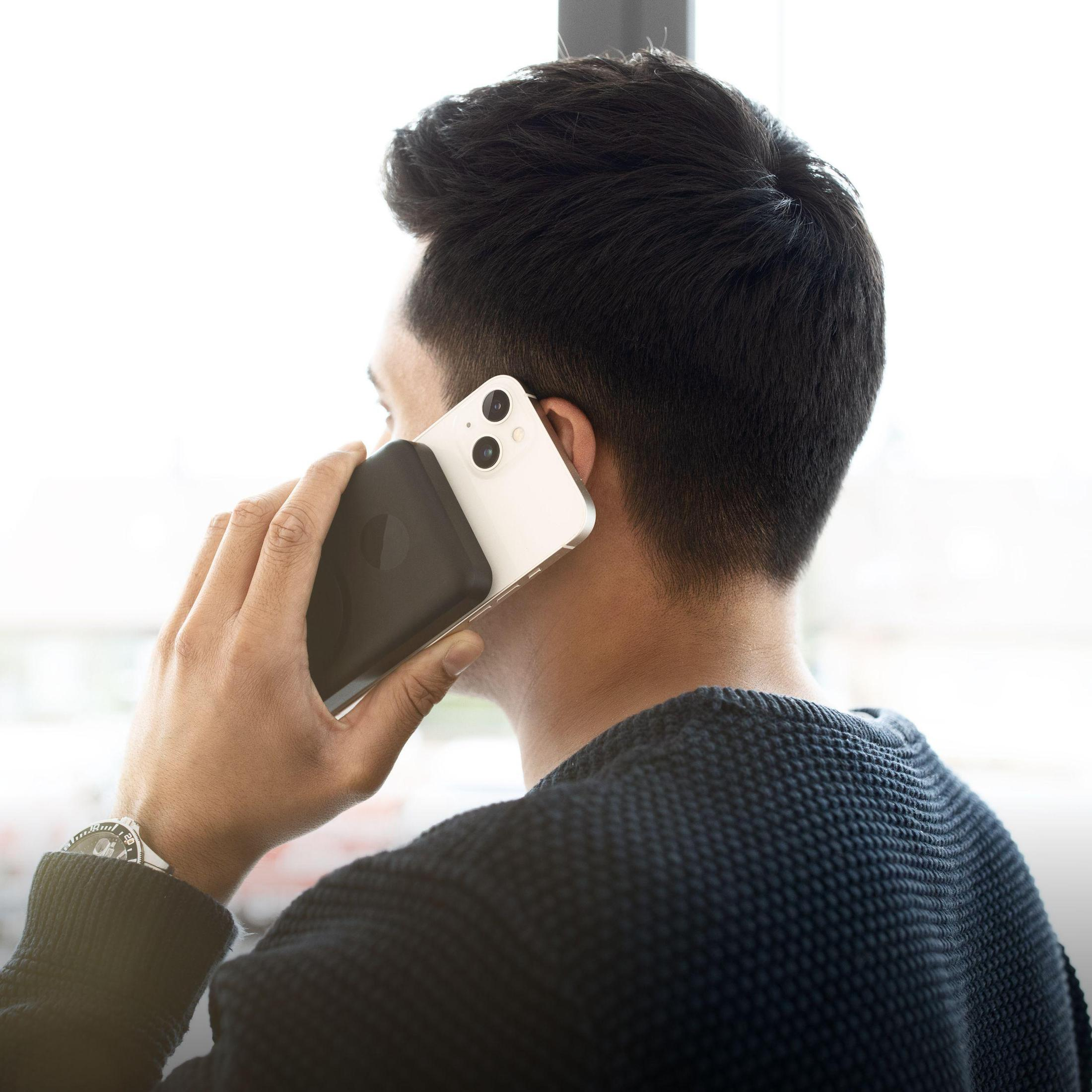 Ein Mann hält ein weißes und schwarzes Telefon an sein Ohr, mit einem Fenster im Hintergrund.