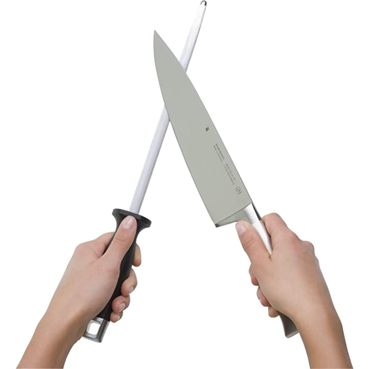 Eine Person schärft ein großes Messer mit einem Wetzstab. Die Hände halten beide Werkzeuge.