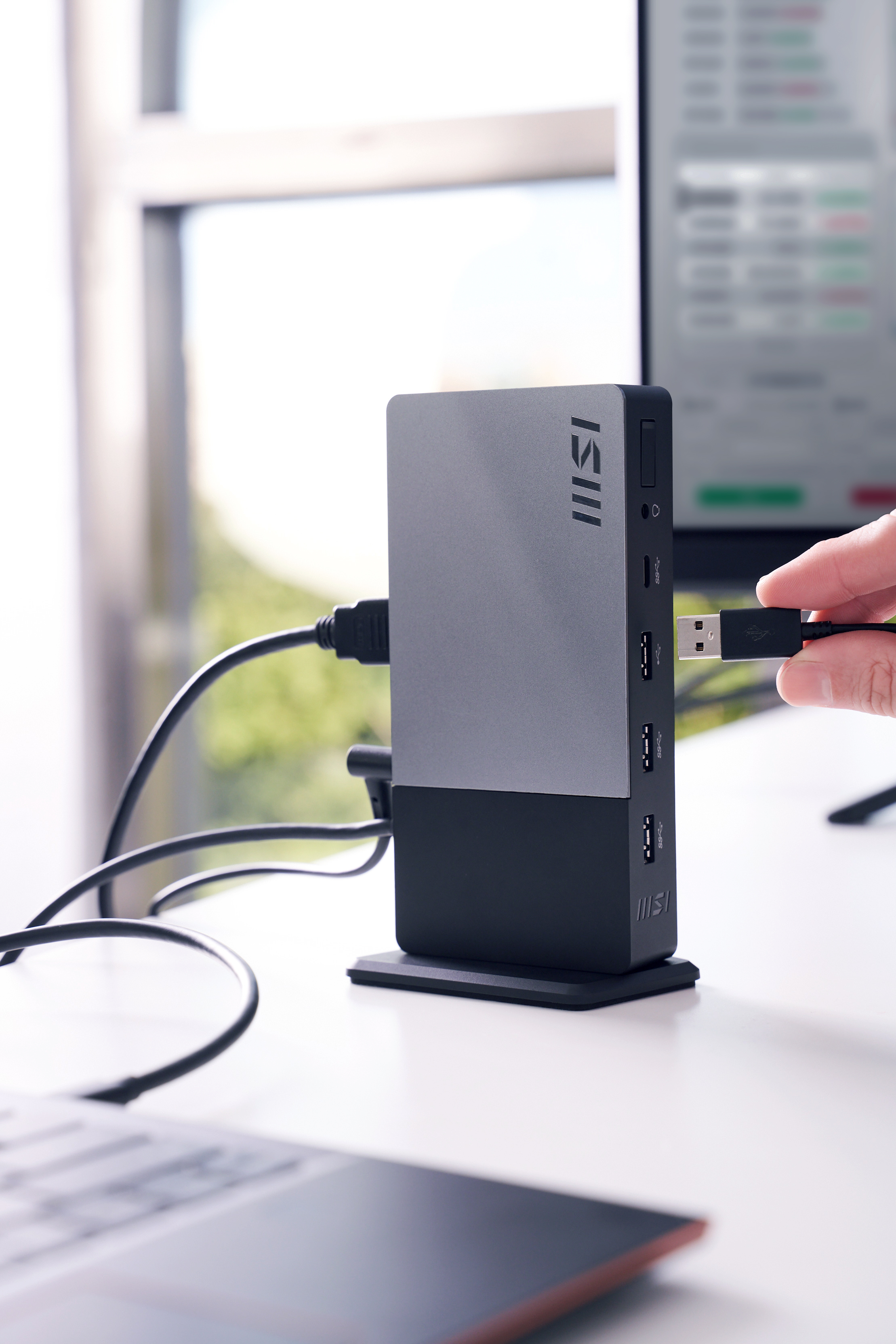 Hub USB argento e nero con cavo USB collegato, su scrivania bianca.