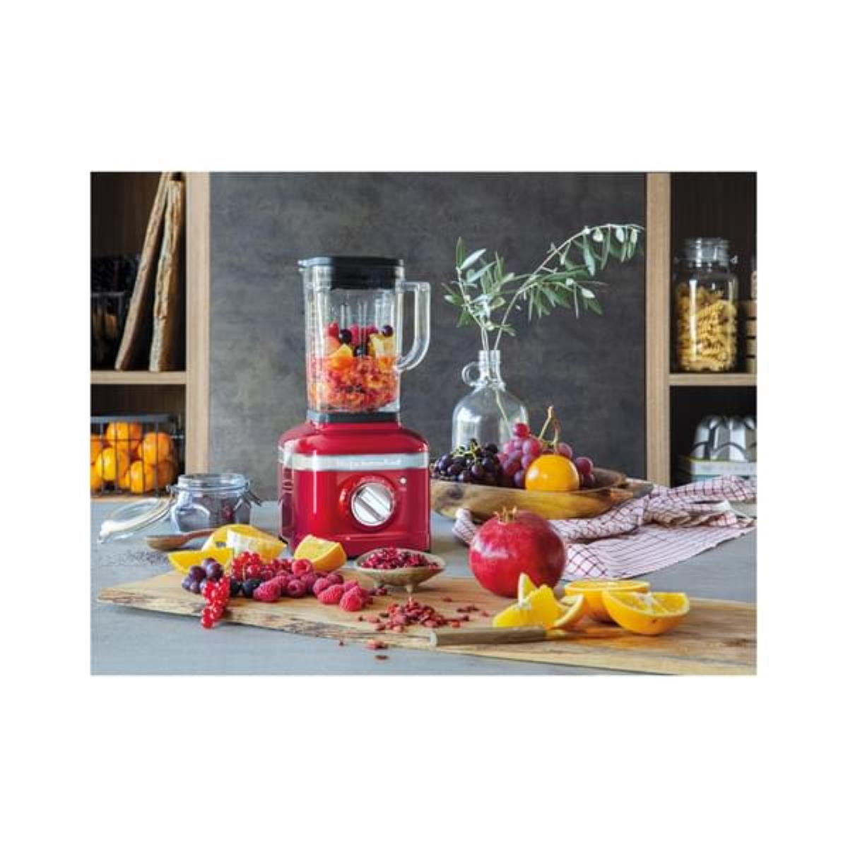 Roter Mixer mit Früchten und Zutaten auf einem Holzbrett.