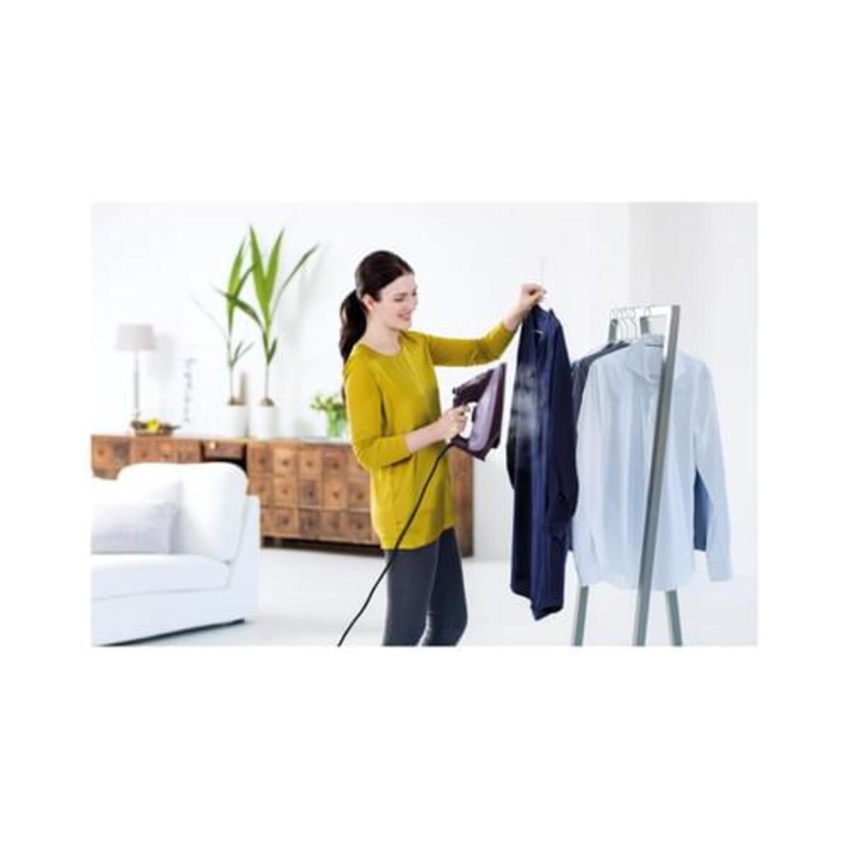 Donna stira vestiti appesi su un'asta in una stanza con divano e mobile.