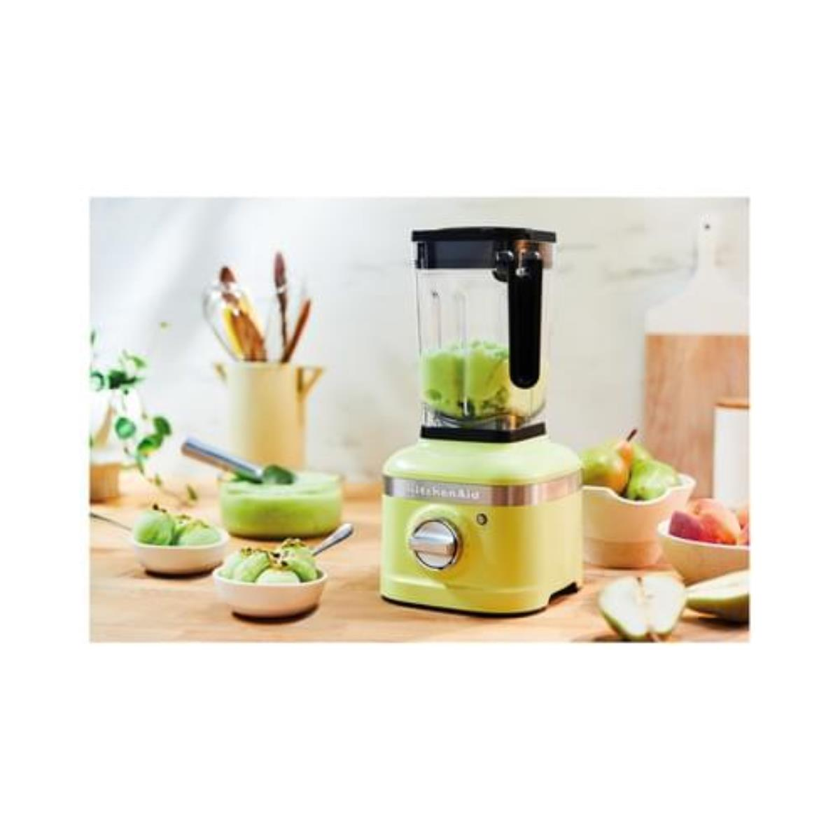 Frullatore KitchenAid verde lime con frullato verde e ingredienti su un tavolo di legno.