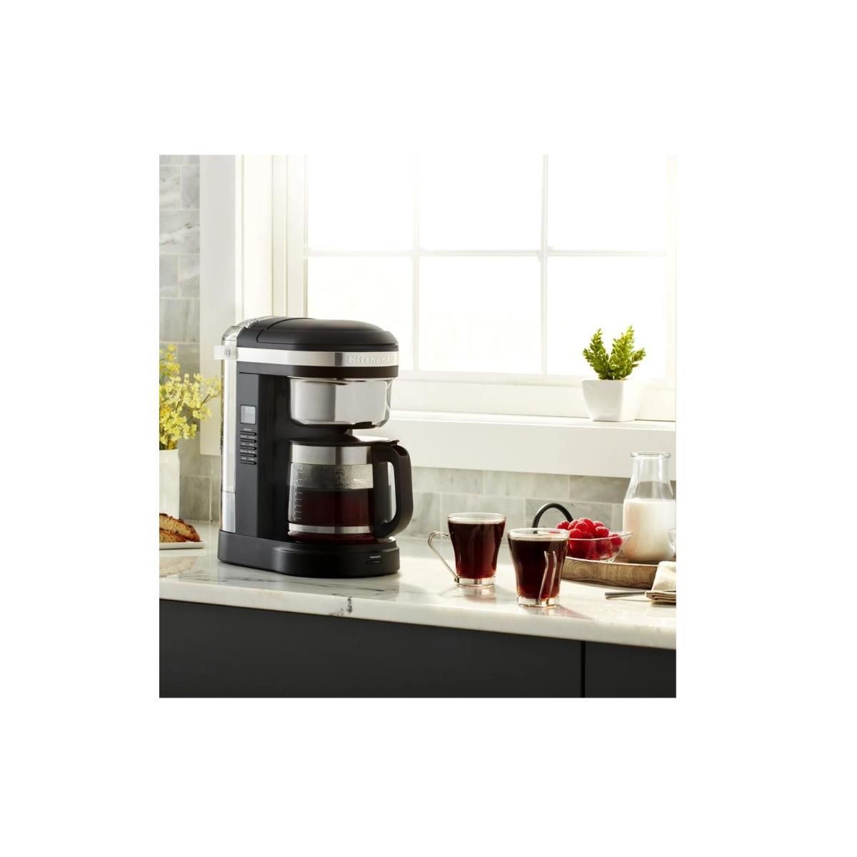 Ekspres do kawy z dwiema filiżankami kawy. Okno w tle. Mleko i chleb również obecne.