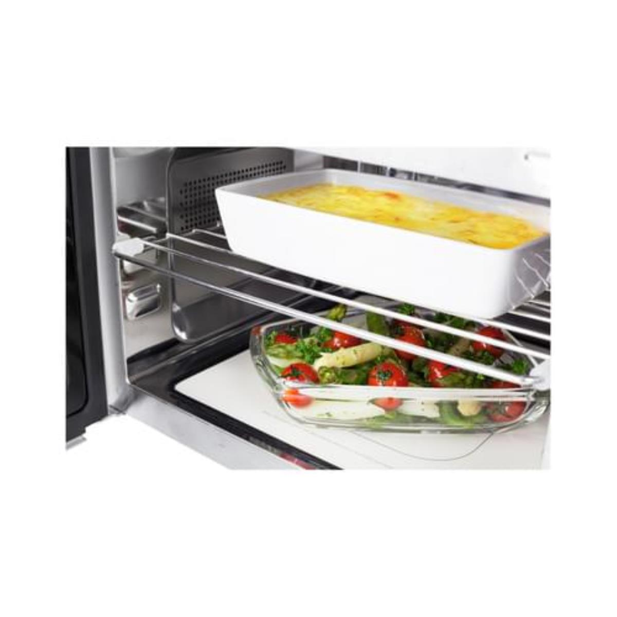 All'interno di un forno moderno con un vassoio di cibo su una griglia. Un altro vassoio sotto con verdure.