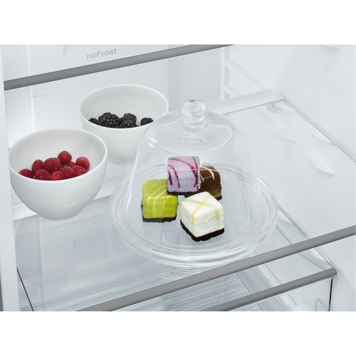 Im Kühlschrank Schalen mit Himbeeren und Brombeeren. Eine Glasplatte mit Gebäck unter einer Haube.