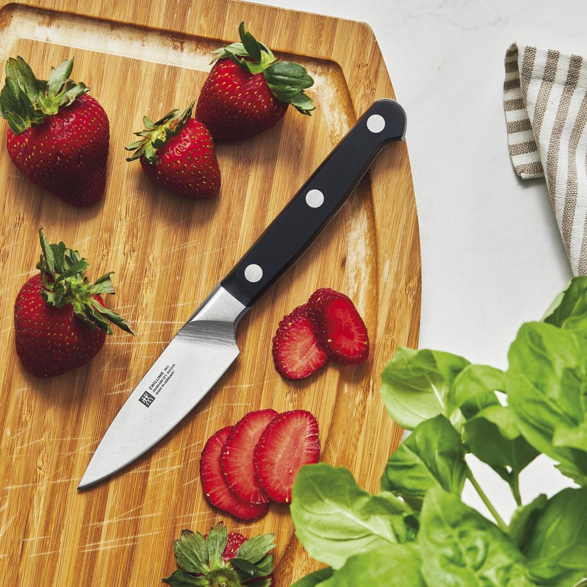 Deska do krojenia z nożem i truskawkami, niektóre pokrojone. Liście bazylii są w rogu.