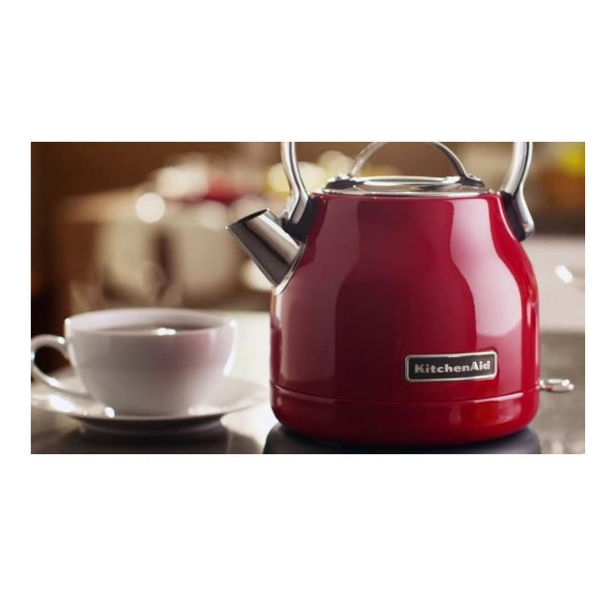 Czerwony czajnik KitchenAid i filiżanka herbaty na stole. Para. Rozmyte tło.