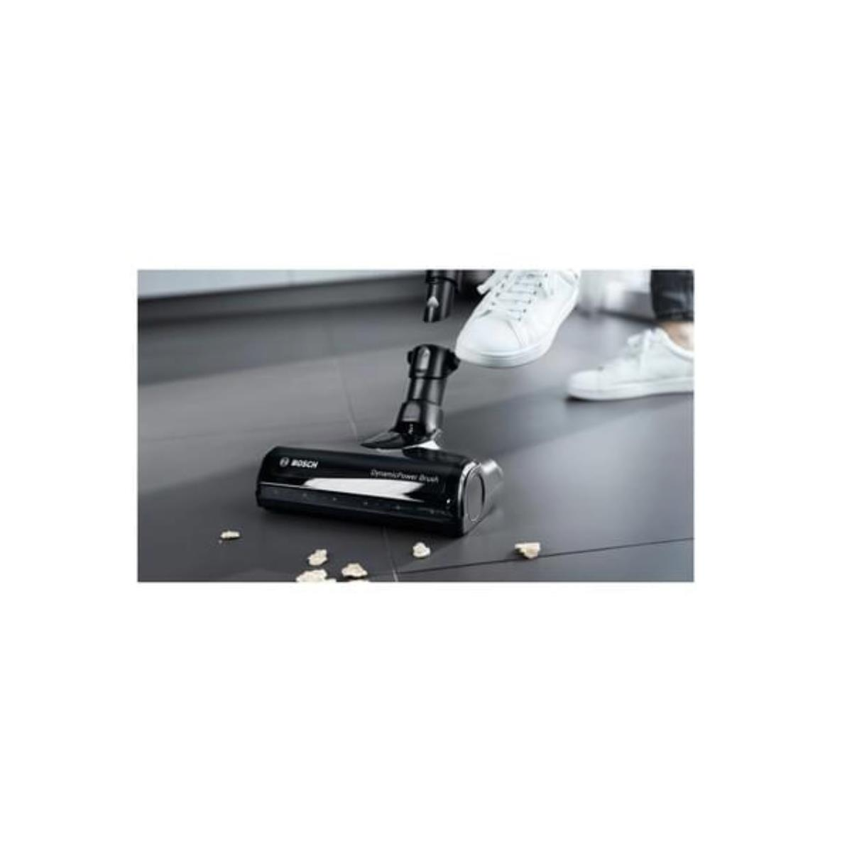 Głowica szczotki odkurzacza na podłodze, wokół rozsypane okruchy.