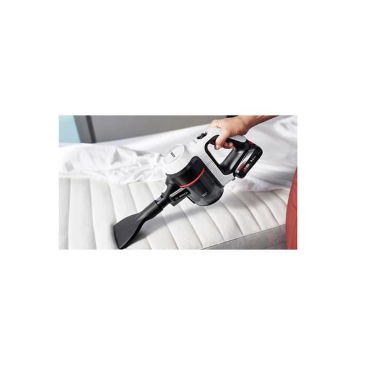 Ręka trzymająca czarno-biały odkurzacz, czyszcząca biały materac.