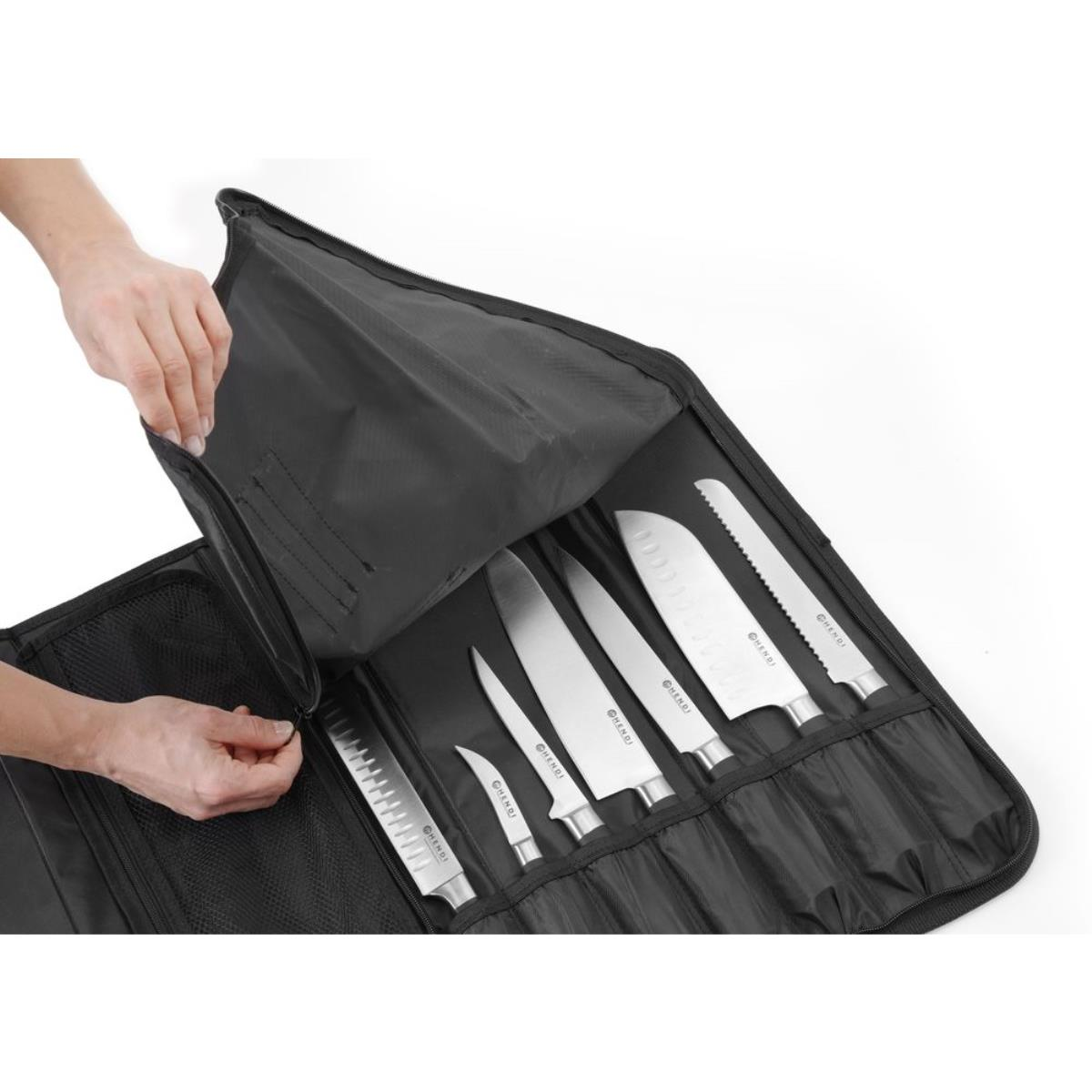 Hand öffnet eine schwarze Messertasche. Messer darin, verschiedene Größen. Weißer Hintergrund.