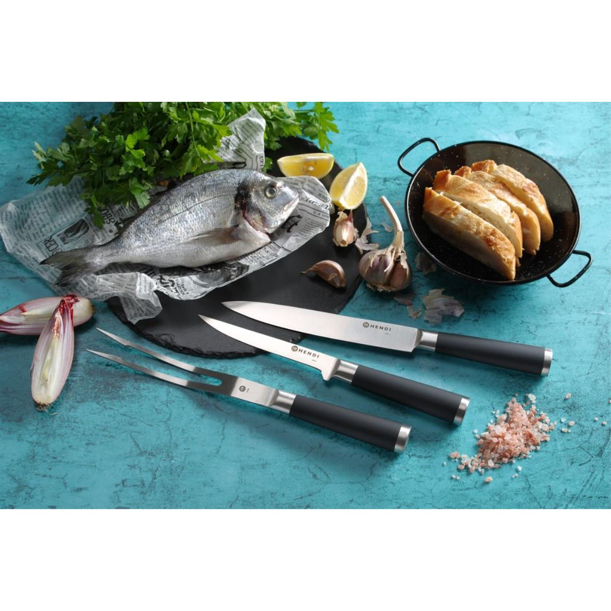 Ein Food-Setup mit Fisch, Brot, Zitronen, Knoblauch und Messern auf dunkler blauer Oberfläche.