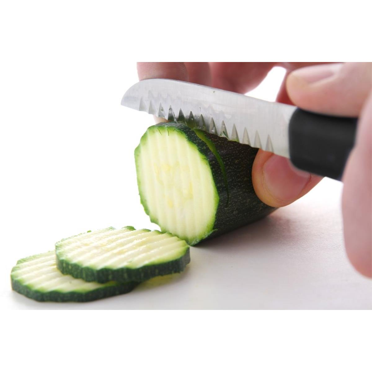 Eine Hand schneidet eine Zucchini mit einem gezahnten Messer auf weißem Grund.
