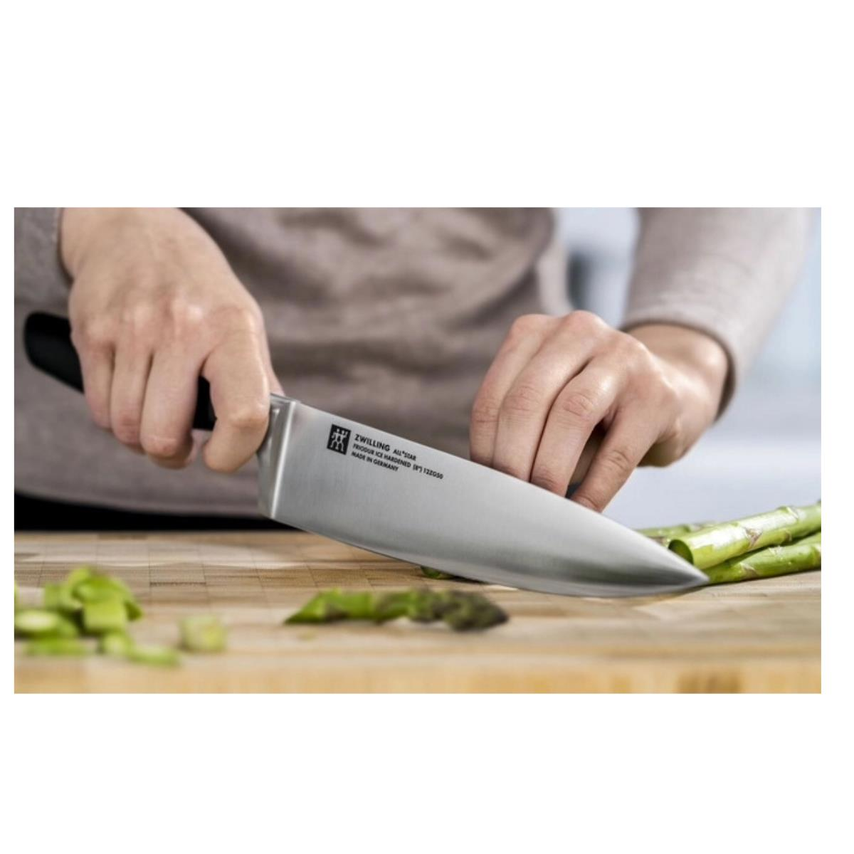 Dłonie krojące szparagi nożem szefa kuchni na drewnianej desce.