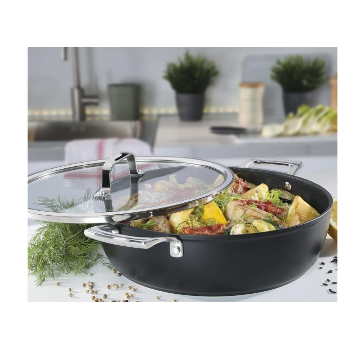 Ein schwarzer Topf mit Essen darin, ein Glasdeckel und ein Küchenhintergrund.