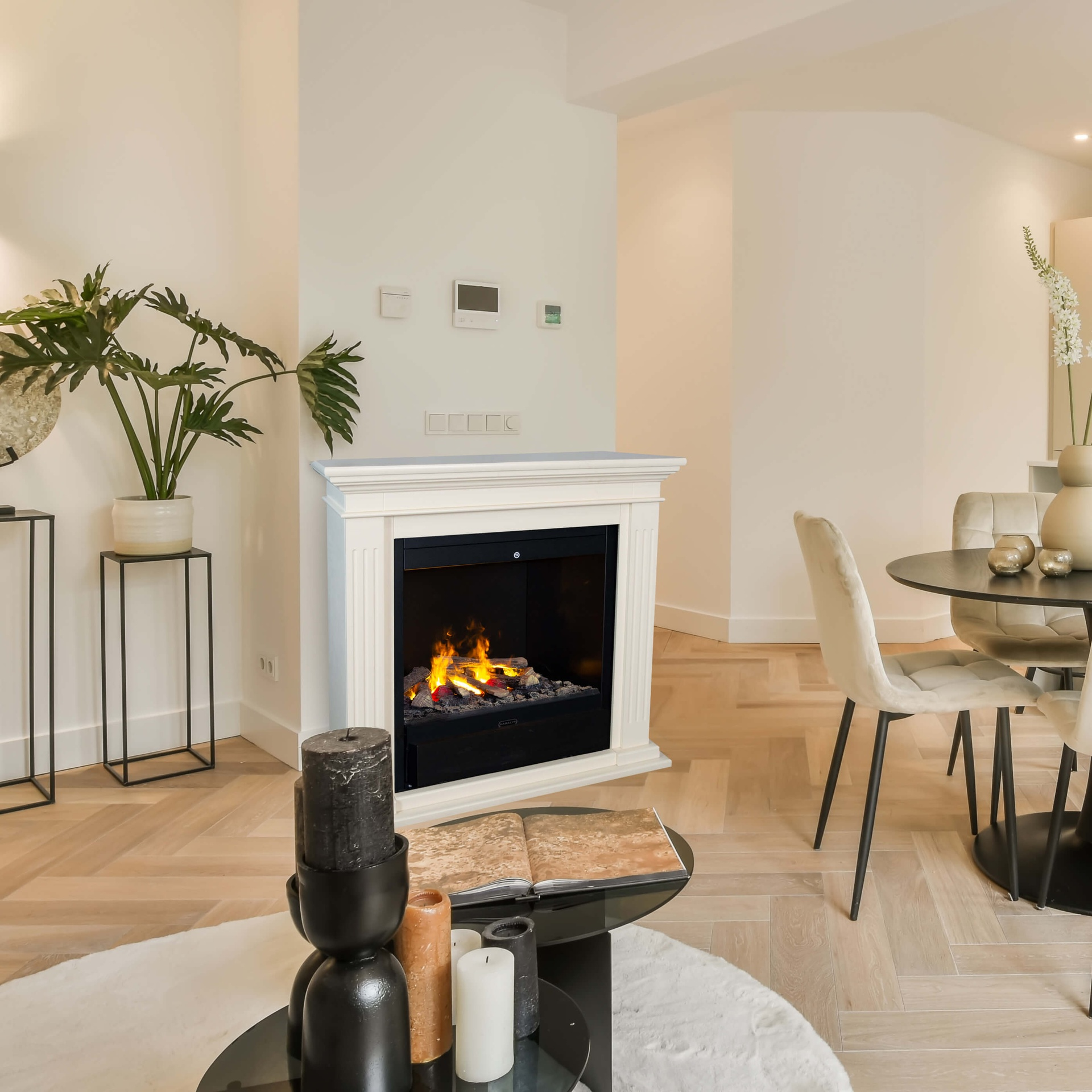 Woonkamer met open haard, kaarsen, salontafel en eettafel met stoelen. De vloer is van hout.