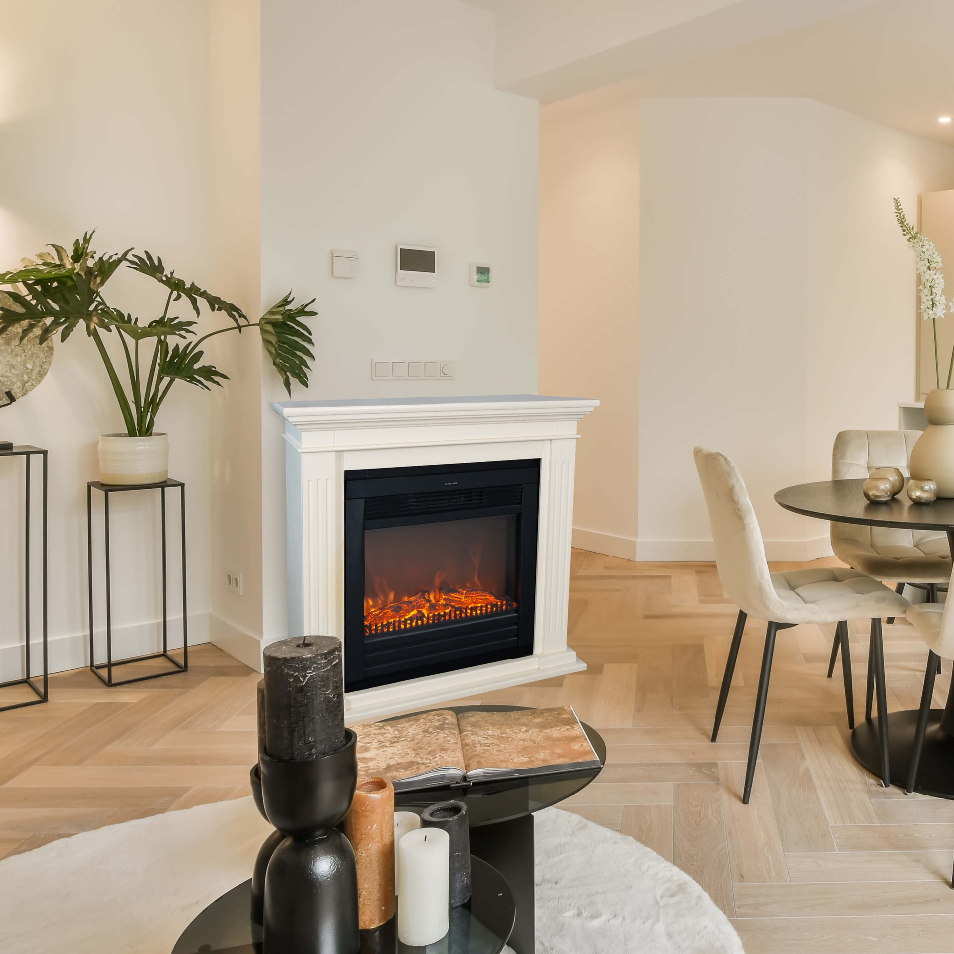 Een woonkamer met een open haard, kaarsen en een eettafel. Neutrale tinten domineren het interieur.
