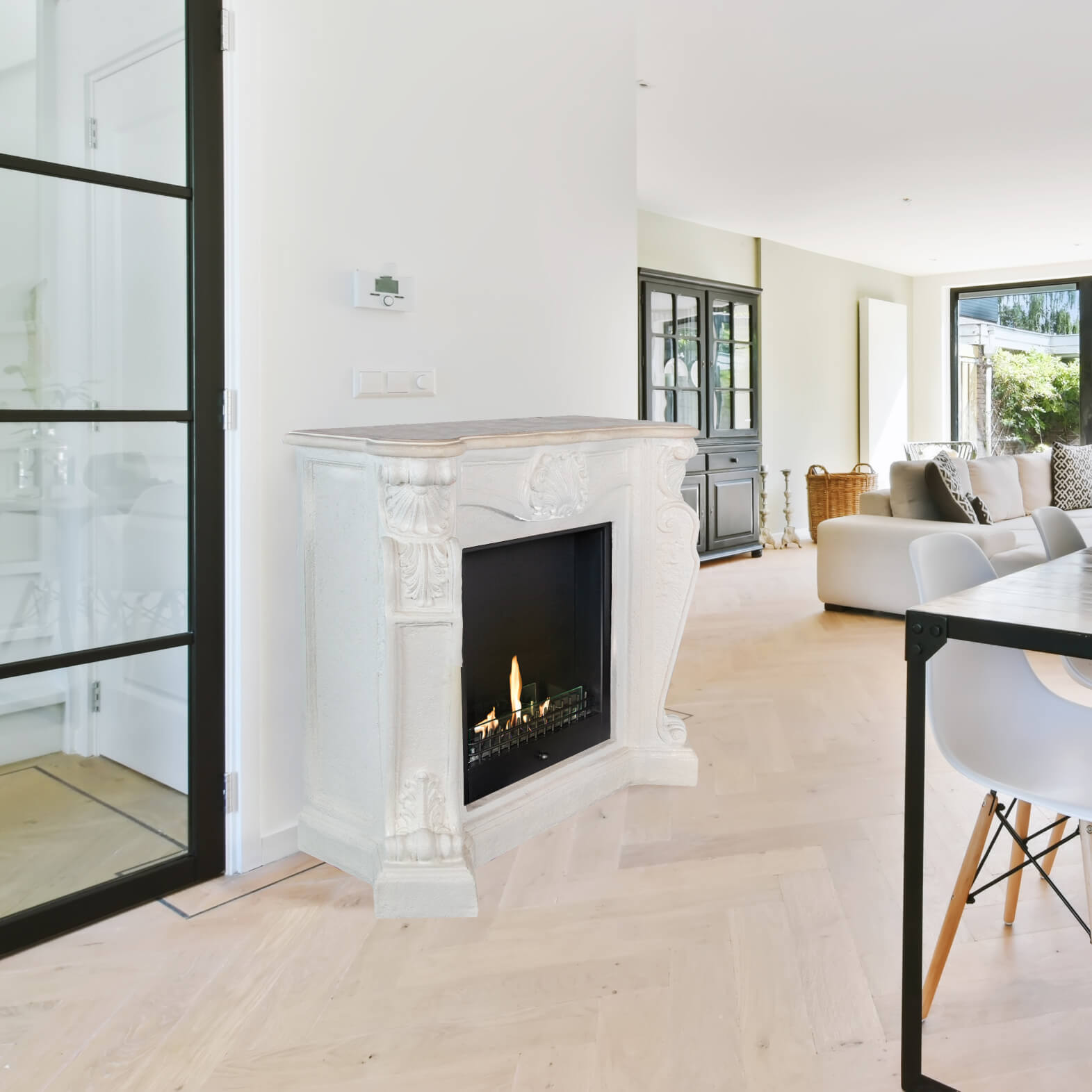 Een kamer met een open haard, een glazen deur en een eettafel. De open haard heeft een zwart interieur met vuur.