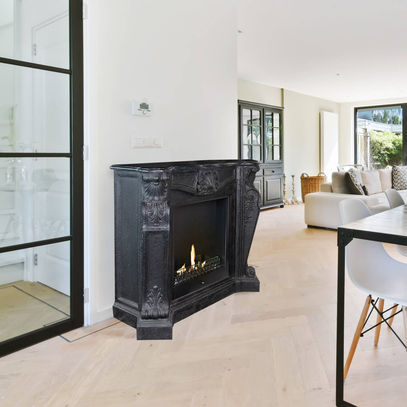 Zwarte open haard met vlammen in een moderne woonkamer met houten vloer. Een bank en tafel zijn zichtbaar.