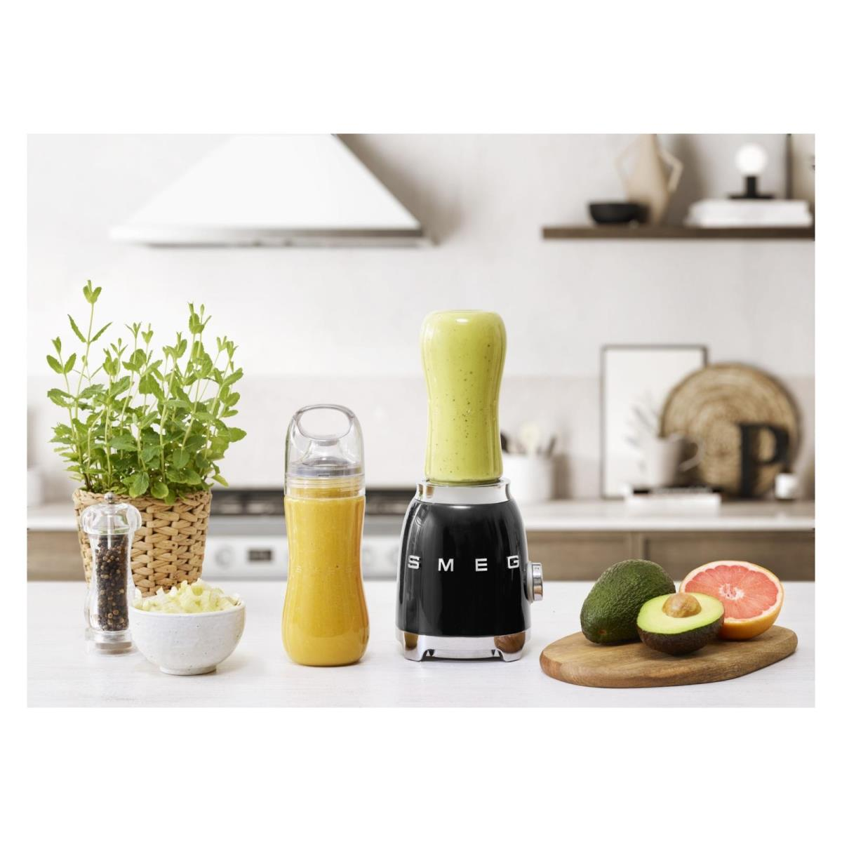 Blender Smeg ze smoothie, awokado, grejpfrutem i rośliną. Biały blat.