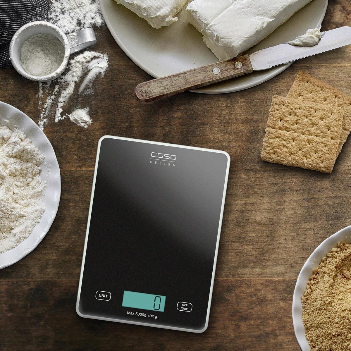 Eine digitale Küchenwaage mit Zutaten wie Mehl, Butter und Crackern auf einem Holztisch angeordnet.