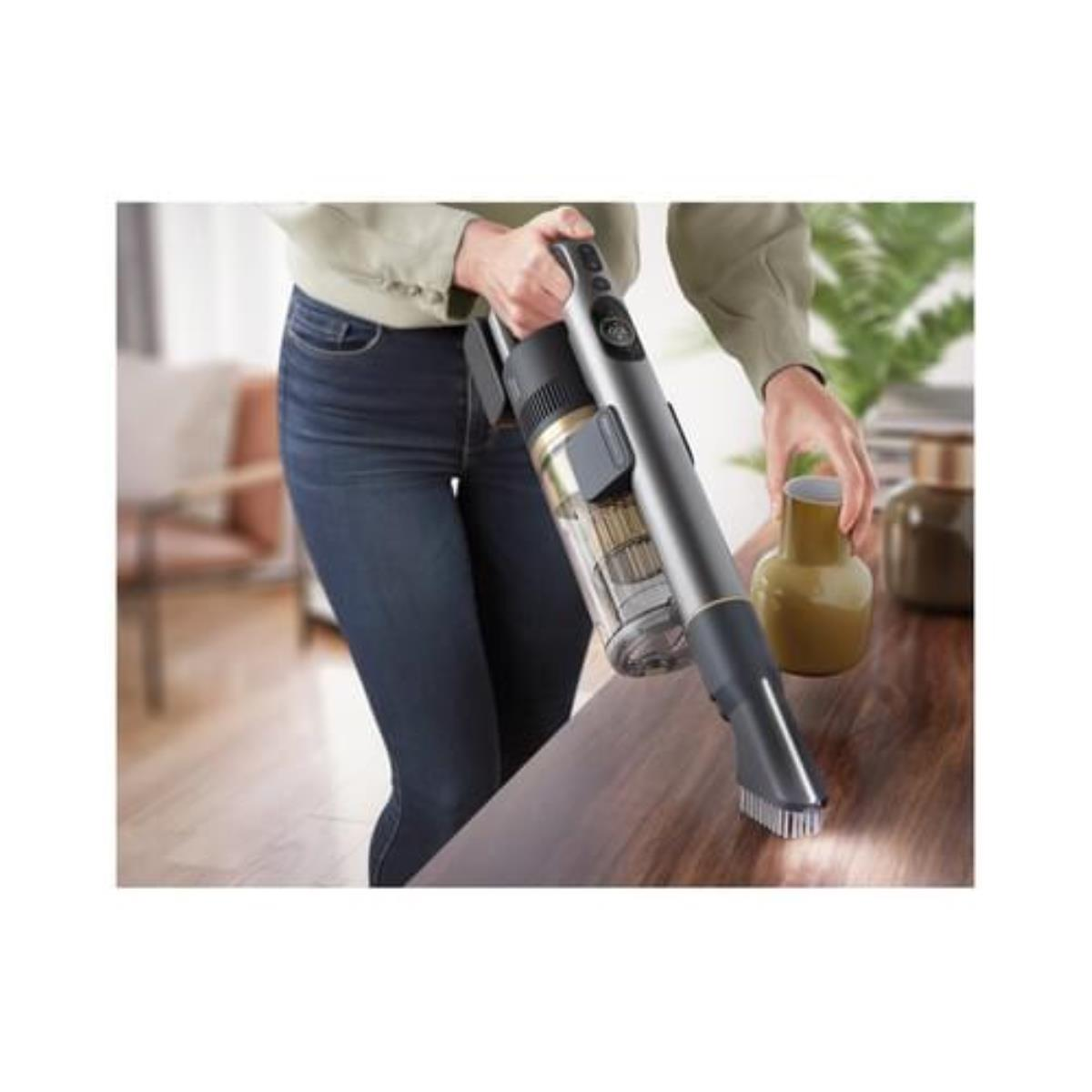 Osoba trzymająca odkurzacz, czyszcząca drewnianą powierzchnię. Waz na prawo.