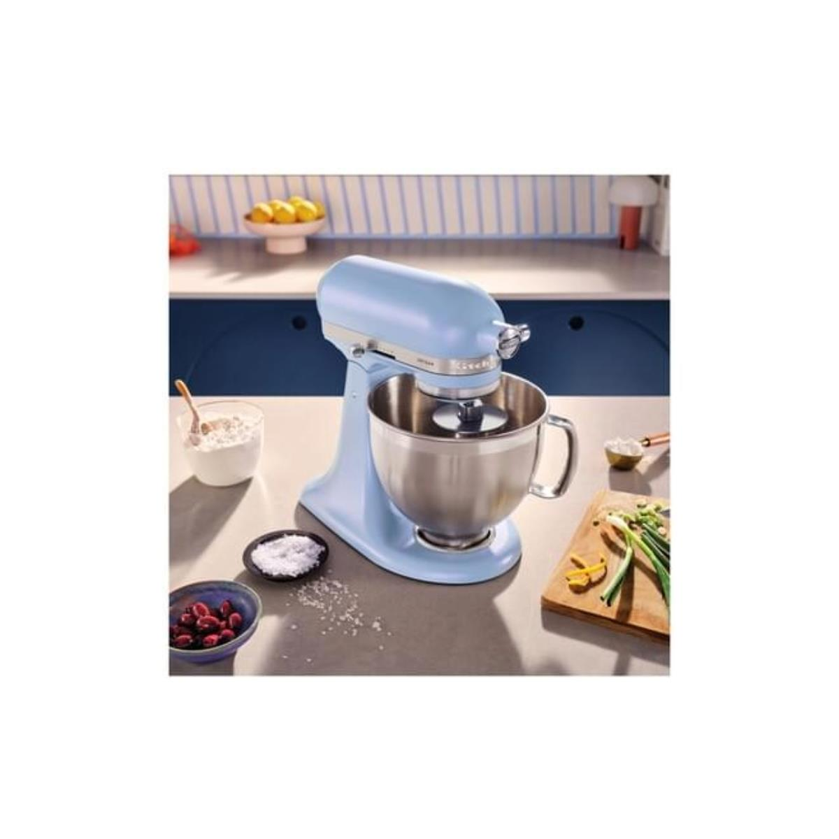 Un'impastatrice azzurra con ciotola in metallo su un piano grigio. Ingredienti come farina e sale vicini.