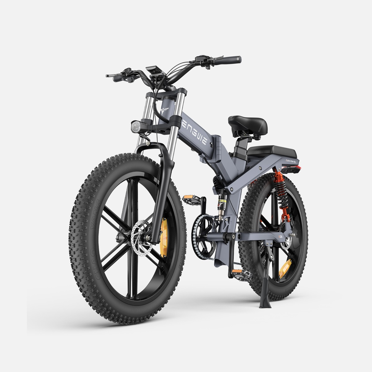 Bicicleta eléctrica gris con neumáticos grandes. Detalles negros y suspensión naranja. Fondo blanco.