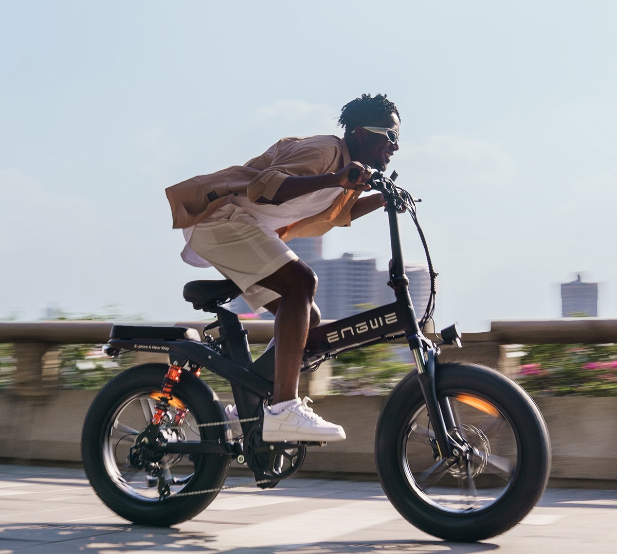 Un hombre montando una bicicleta eléctrica Engwe negra en un día soleado.